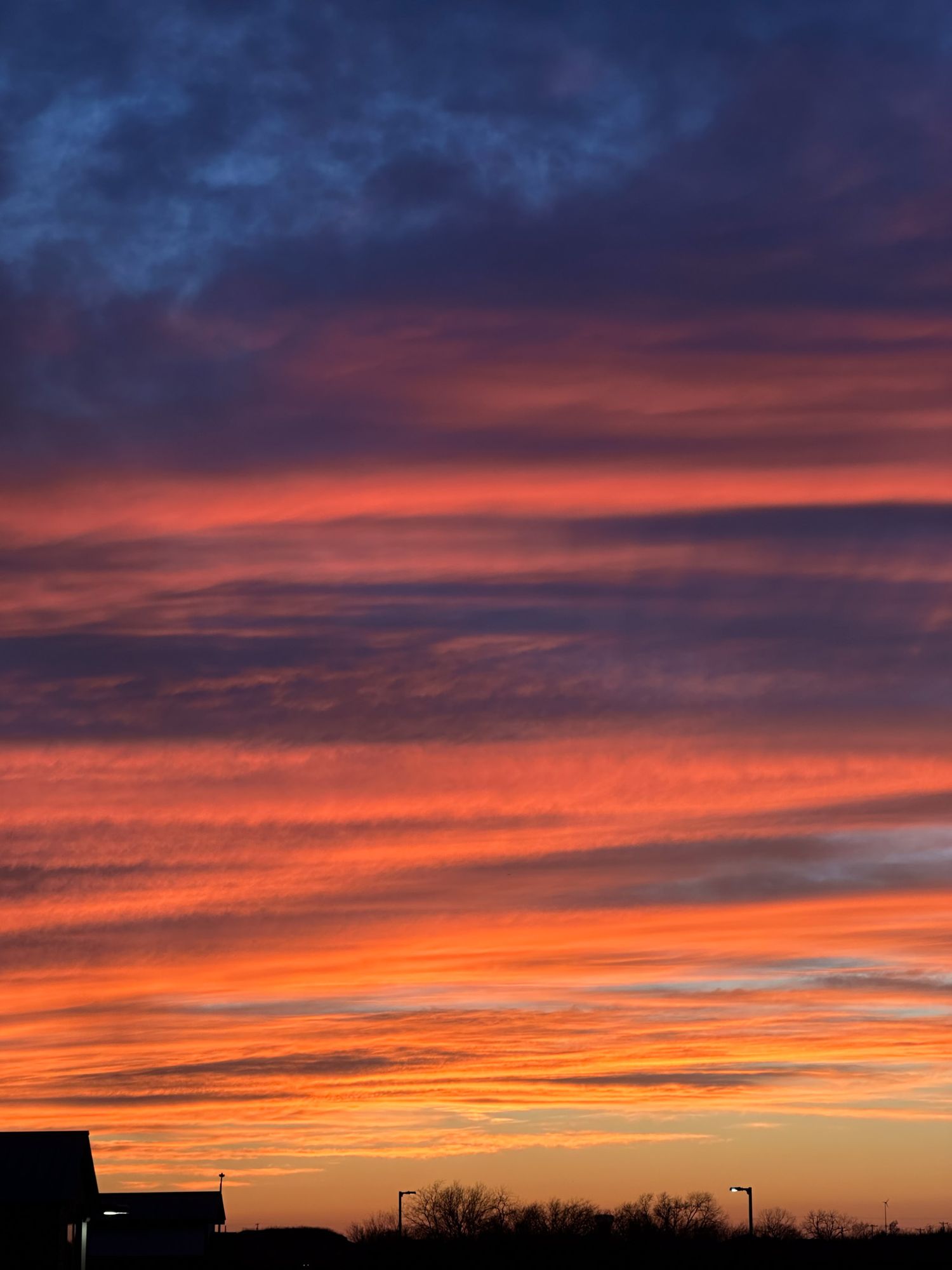 Vibrant orange and purple clouds paint the sky during a dramatic sunset over a dark silhouetted landscape.