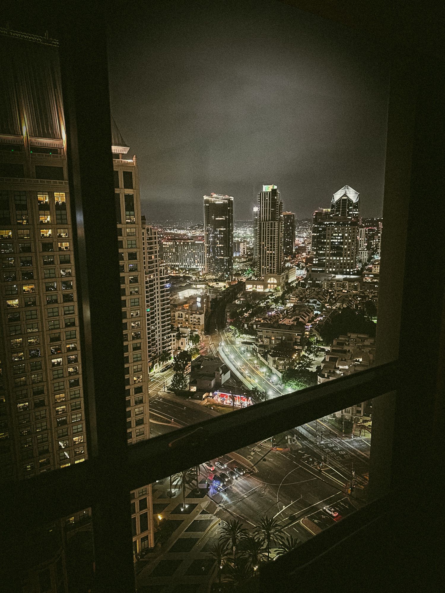 Dramatic cityscape view at night showing illuminated high-rise buildings and roads from an elevated vantage point.