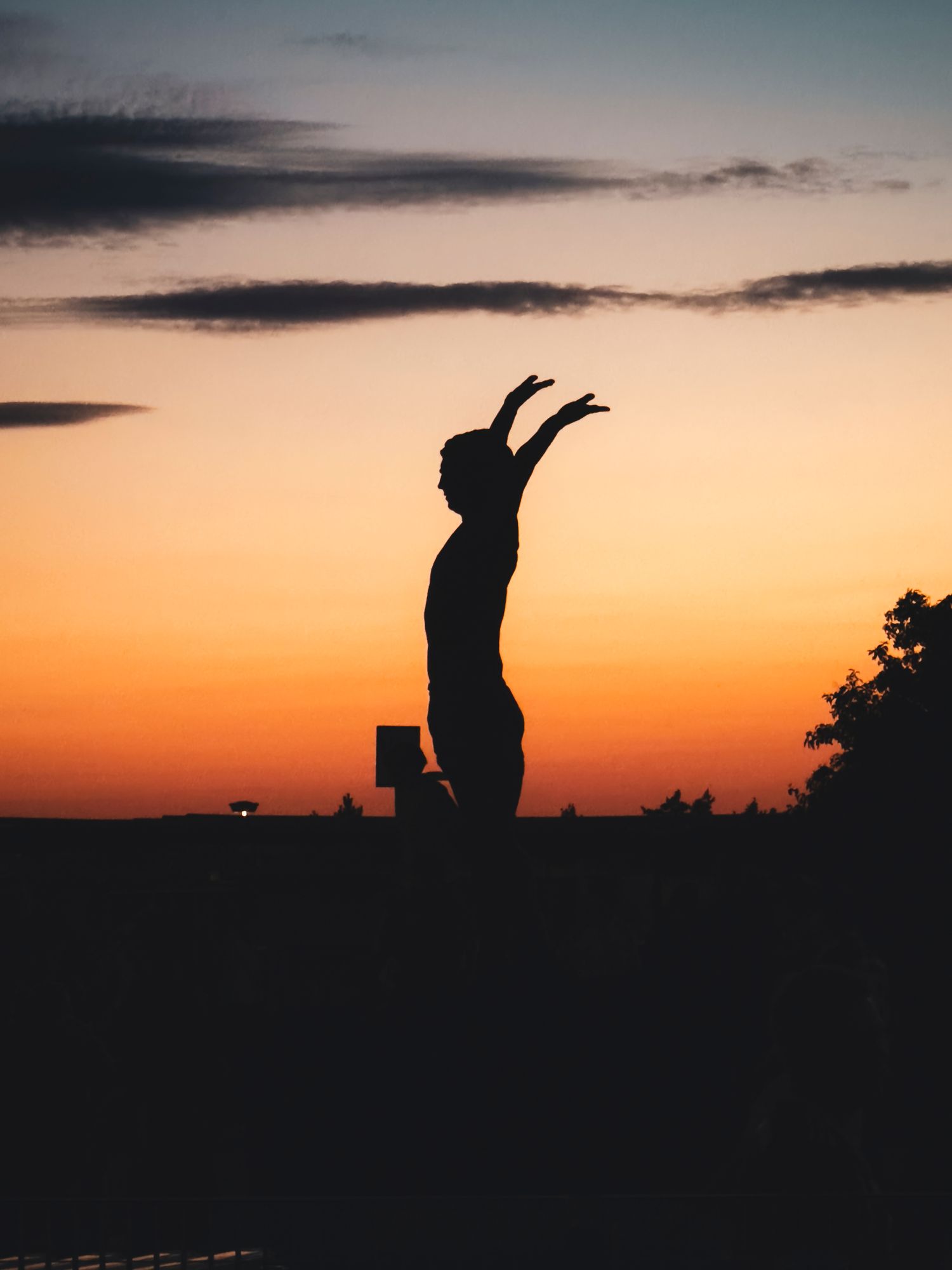 Silhouette of the Franz Beckenbauer statue outside the Allianz Arena in Munich, Germany, captured against a vibrant sunset sky.