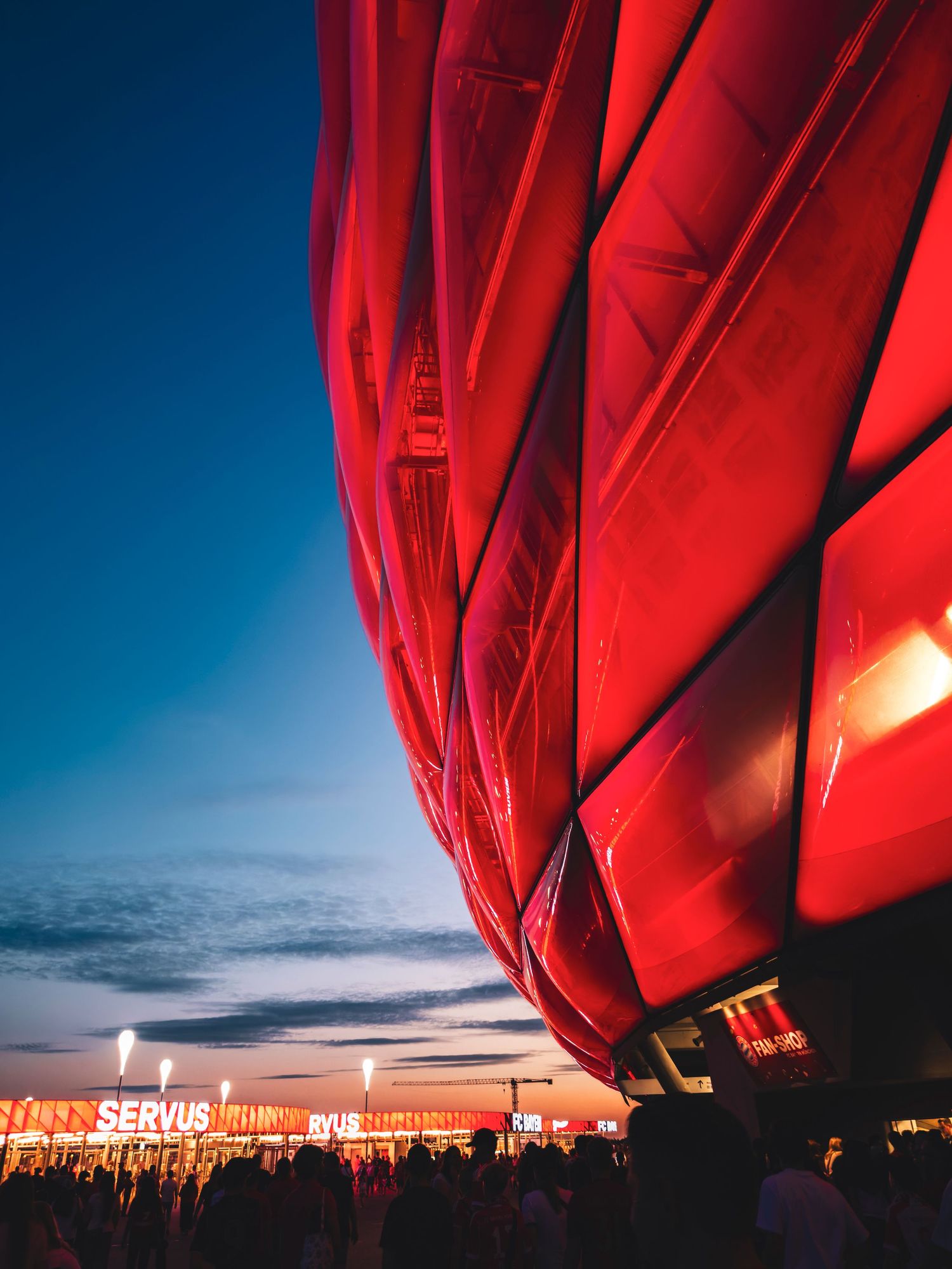 The exterior of the Allianz Arena in Munich, Germany, famously illuminated with bright red panels at dusk.