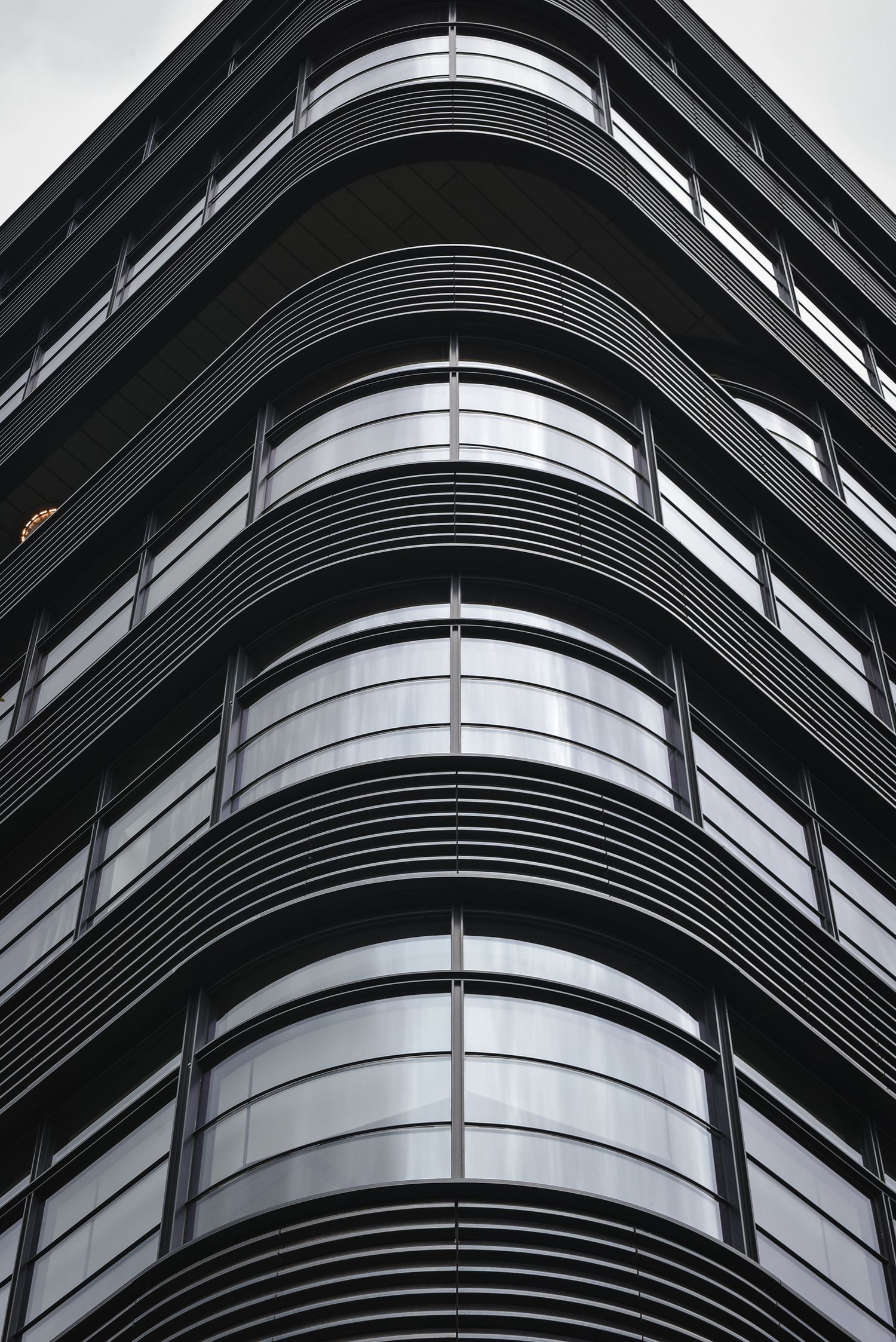 Modern curved building facade in New York City, featuring sleek black metal siding and large rounded glass windows.