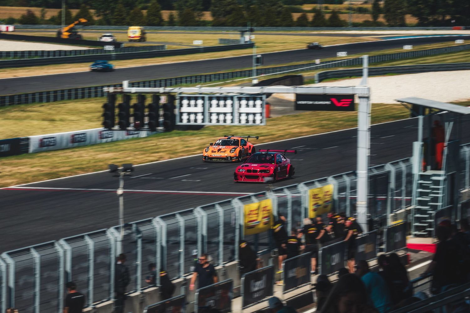 High-angle view of GT race cars passing the start-finish gantry at the Slovakia Ring circuit in Orechová Potôň, Slovakia.