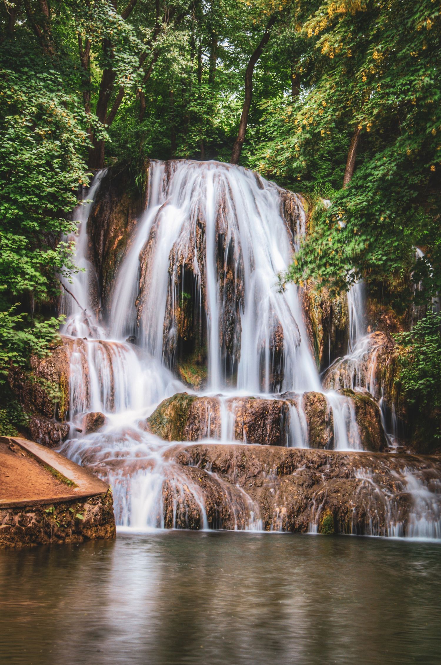 Lučanský vodopád (Lúčky Waterfall) in Slovakia, featuring smooth cascading water surrounded by lush green forest foliage.