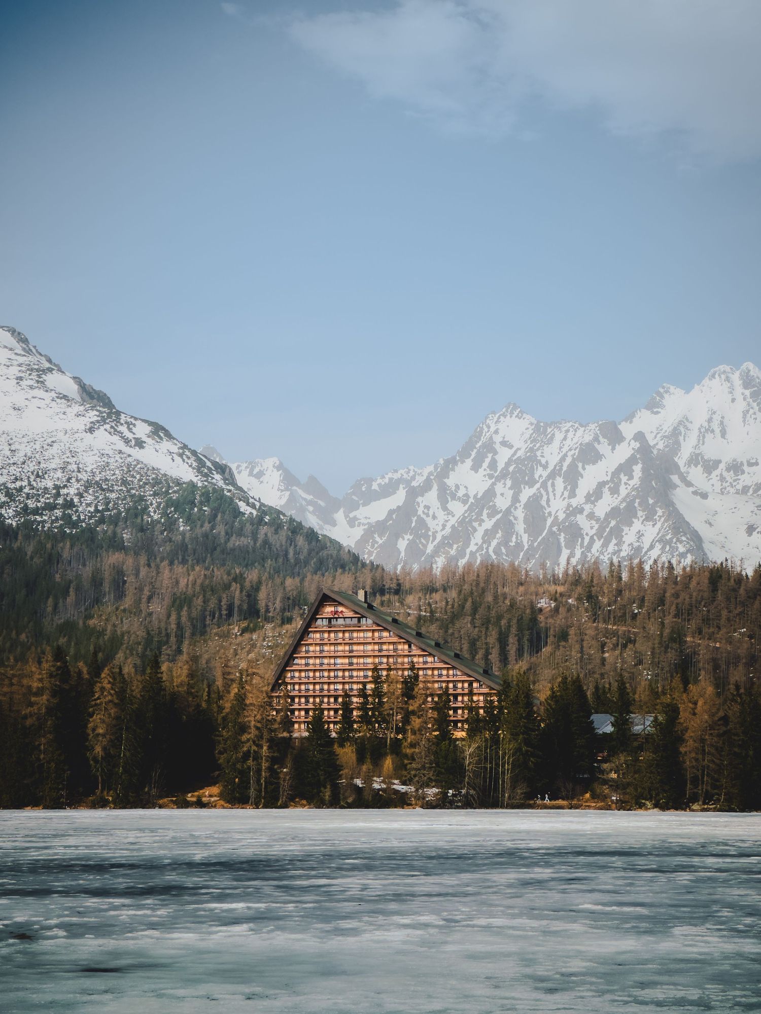 Iconic Hotel Patria on the shore of frozen Štrbské pleso in the High Tatras, Slovakia, backed by snow-capped mountains.