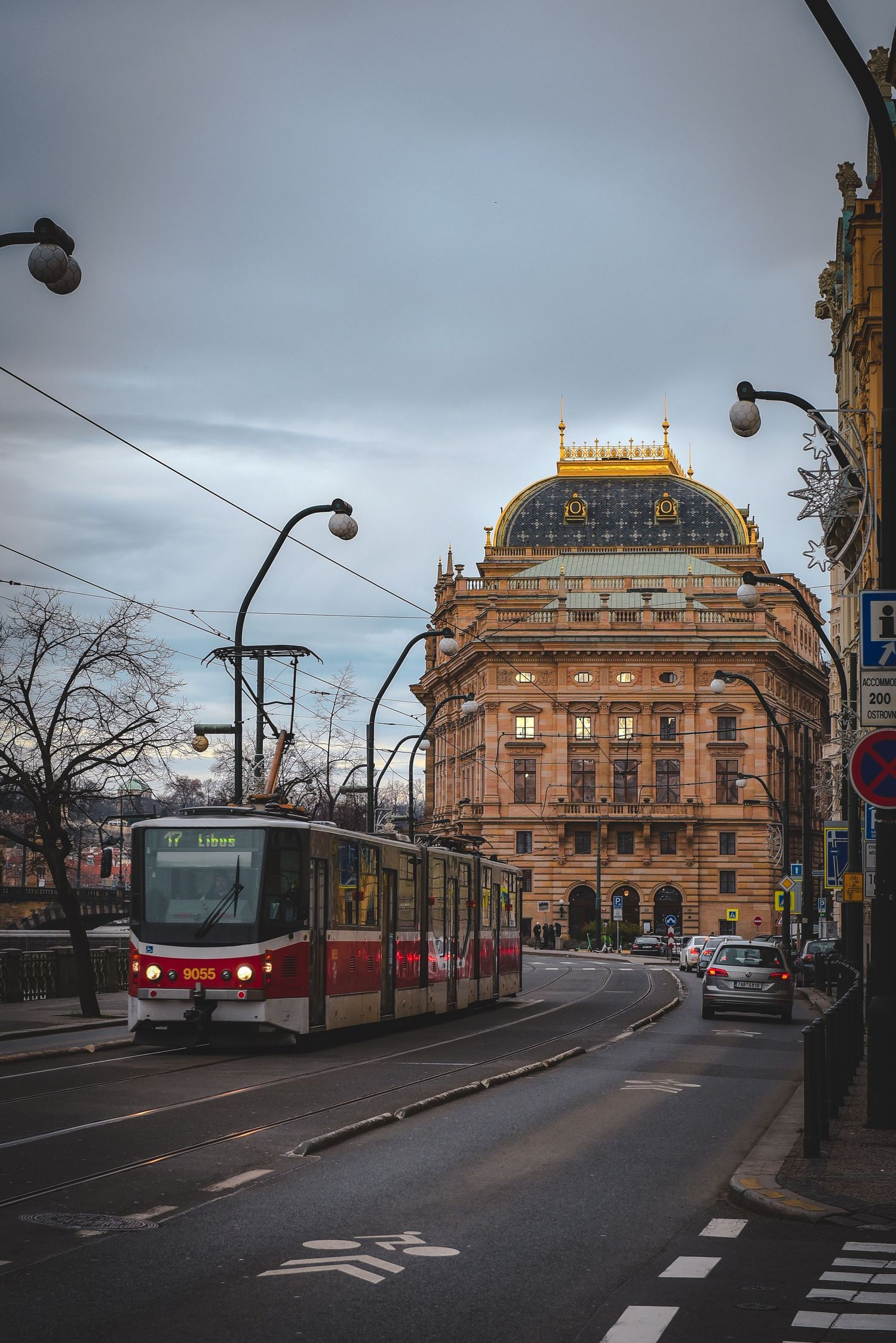 A classic red public transit tram driving past the historic National Theatre building in Prague, Czech Republic.