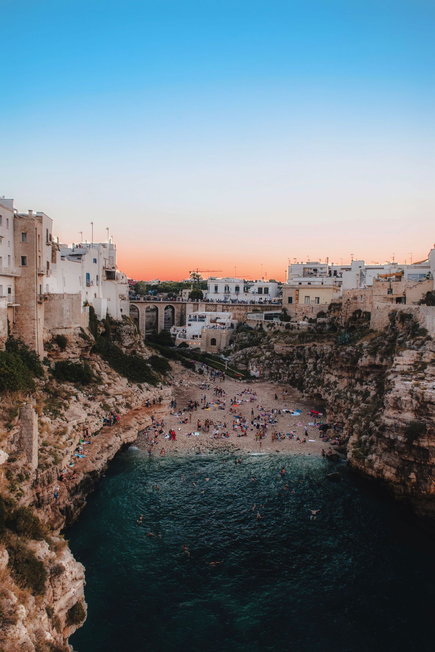 Famous Lama Monachile beach and cove in Polignano a Mare, Italy, surrounded by cliffs and historic buildings at sunset.