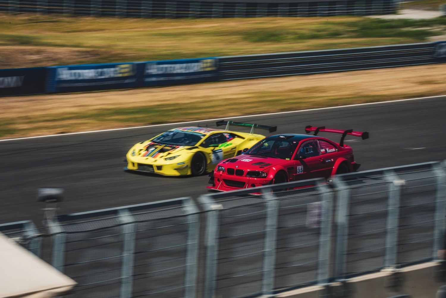 Red BMW GT car and yellow Lamborghini GT3 racing side-by-side on the main straight at Slovakia Ring in Orechová Potôň, Slovakia.