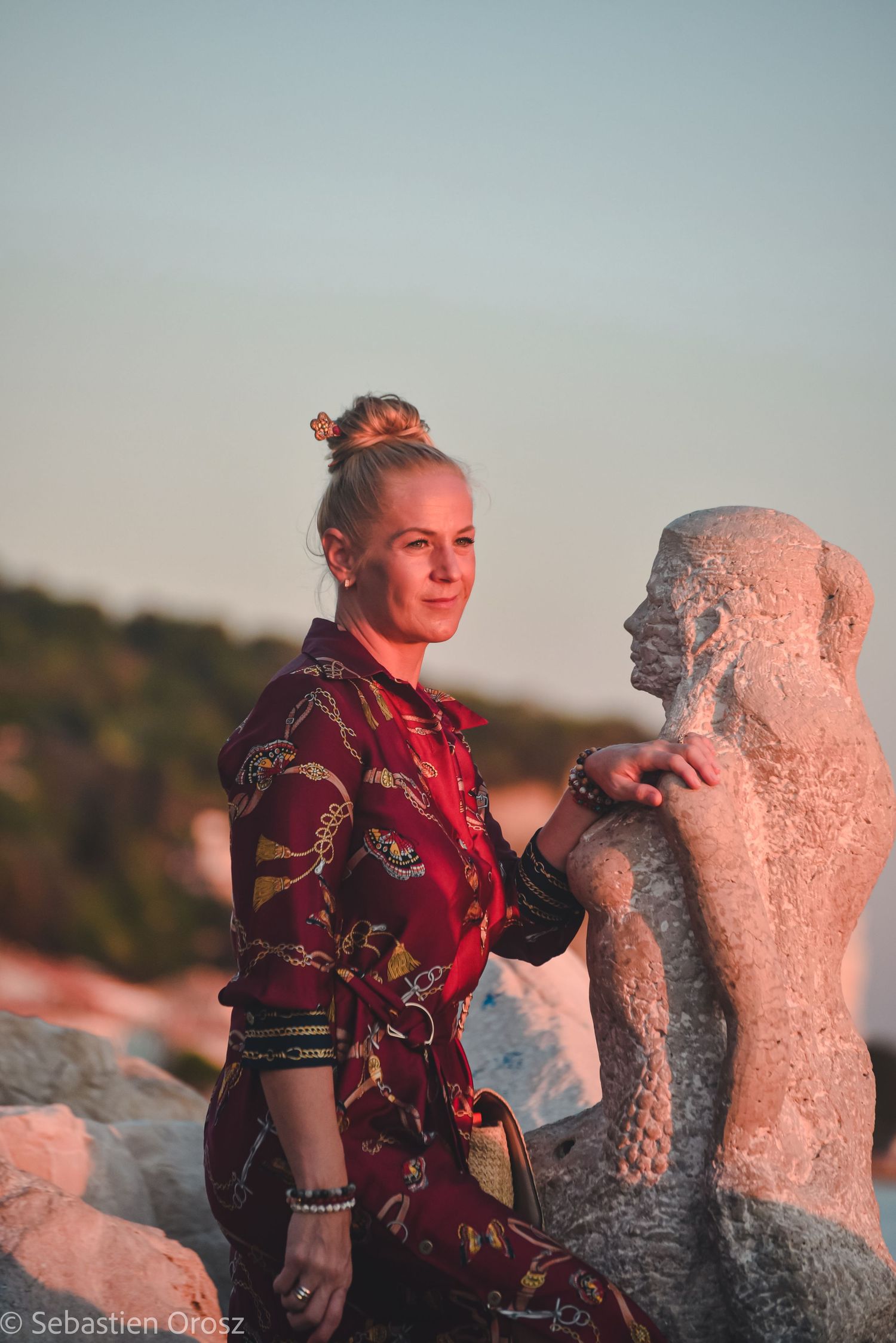 Sunset profile portrait of a woman posing next to a coastal stone statue in Piran, Slovenia.