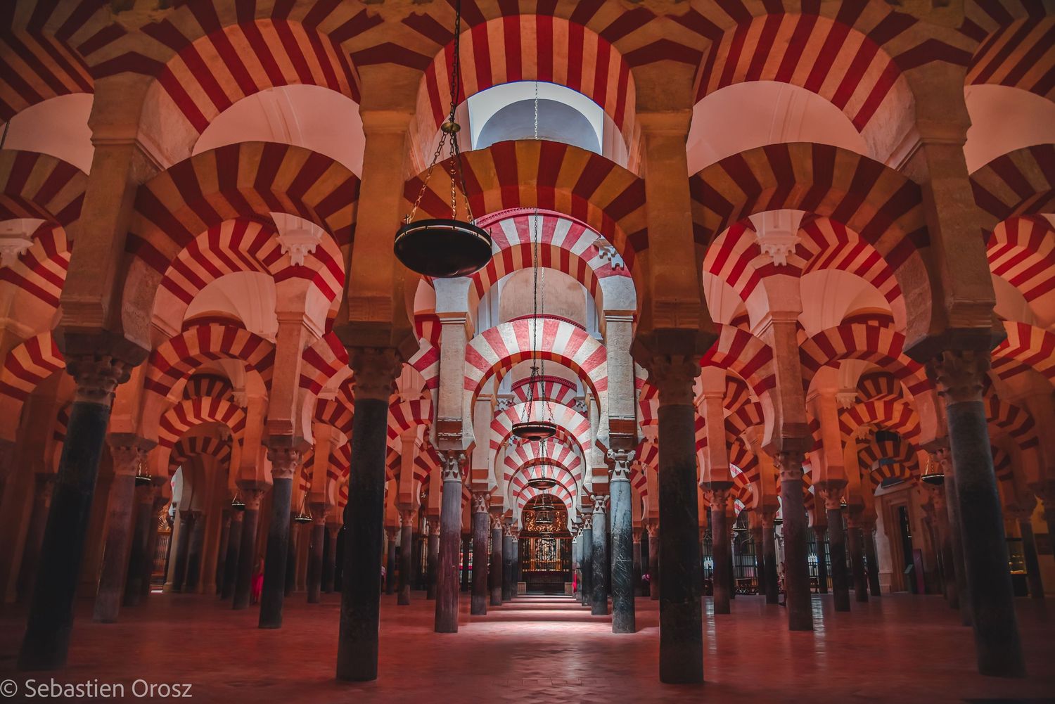 Interior of the Mosque-Cathedral of Córdoba in Spain, featuring its iconic red and white striped arches and historic columns.