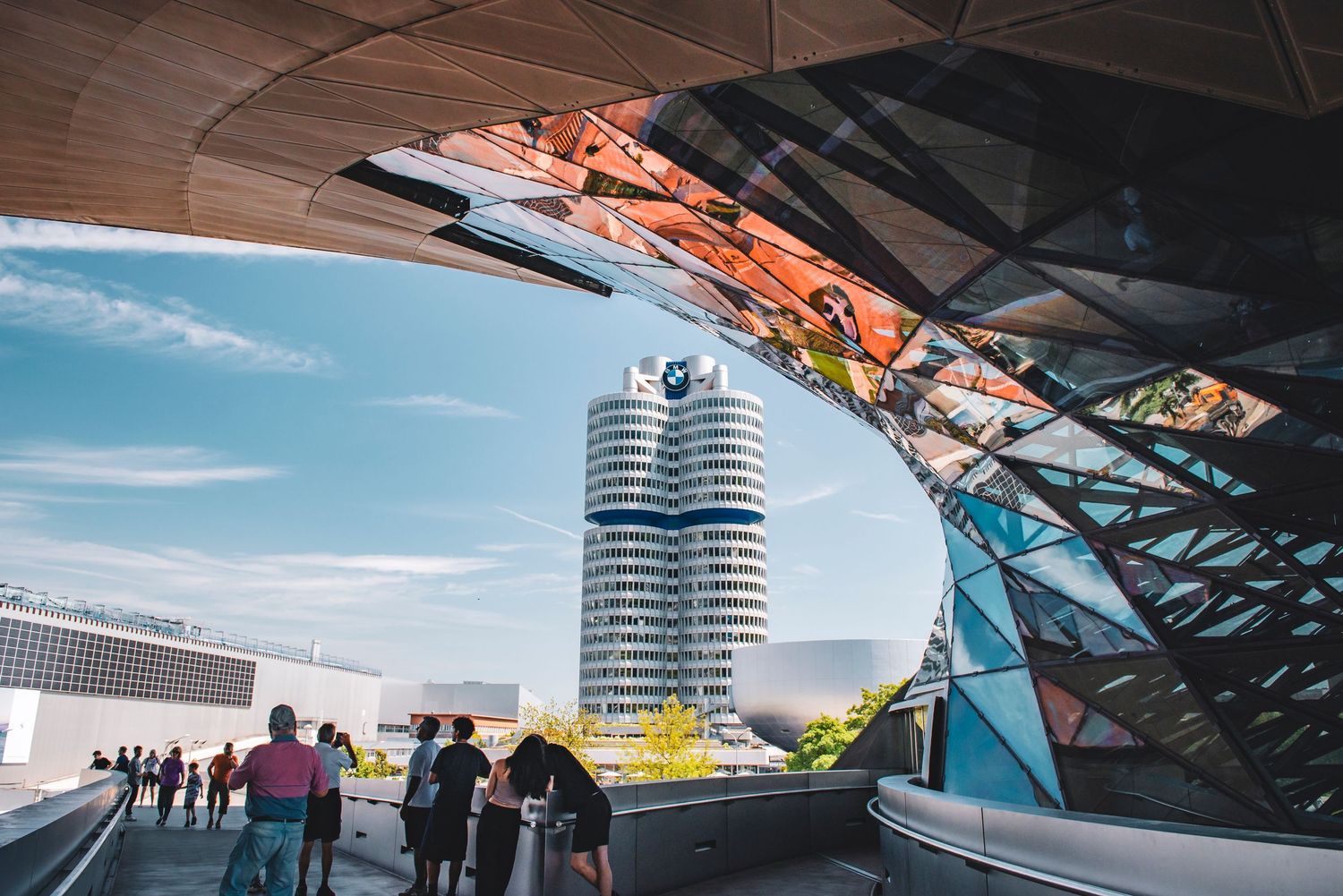 View of the BMW Headquarters tower in Munich, Germany, framed by the modern architecture and reflective glass of BMW Welt.