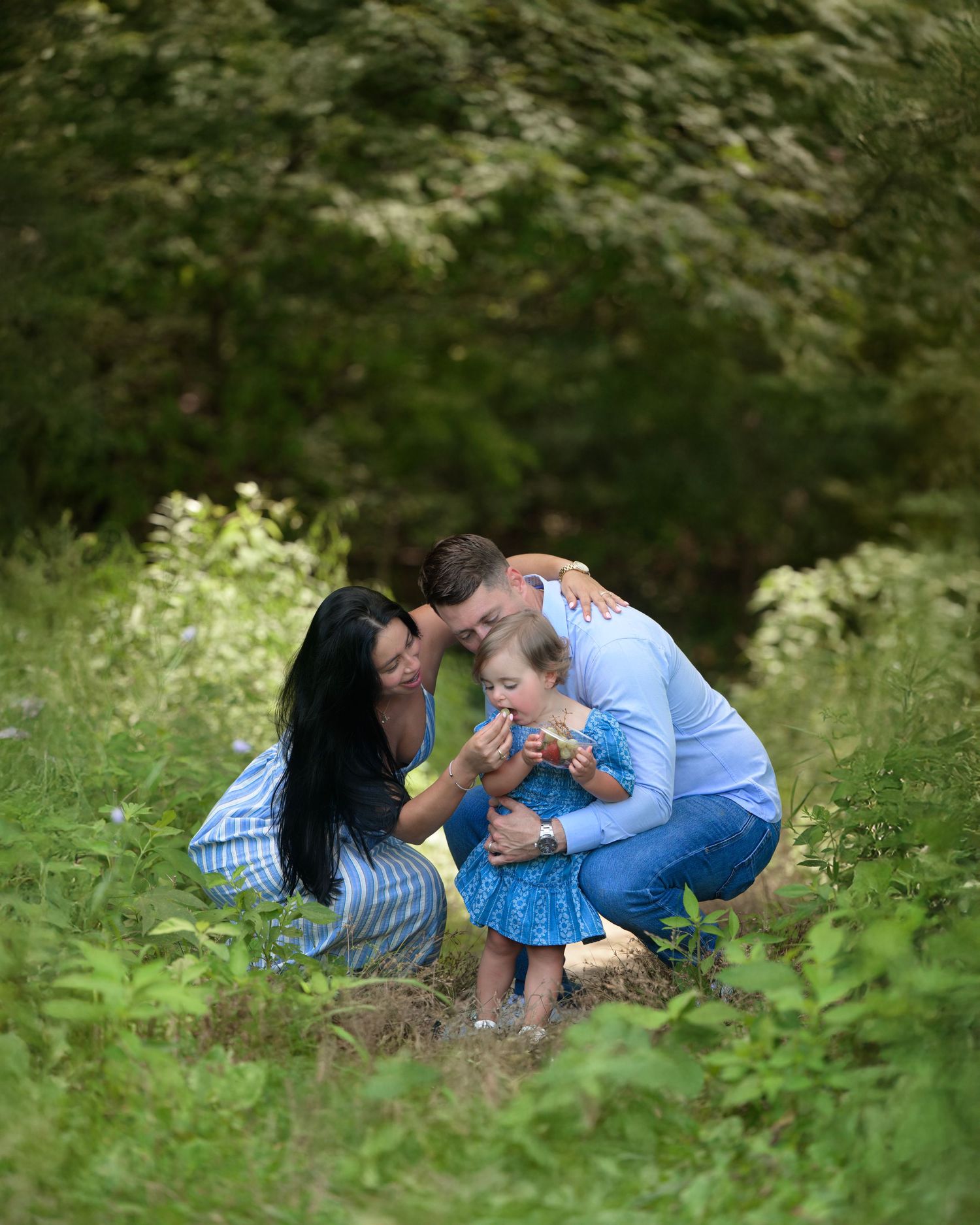 A family plays together and shares joyful moments while lying in a grassy meadow on a sunny day.