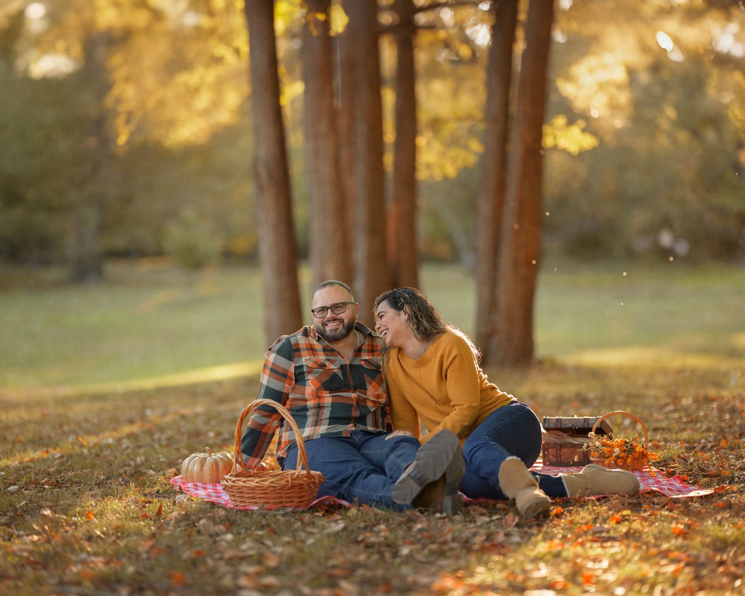 Couple enjoying an autumn picnic on fallen leaves in a park during golden hour sunset.