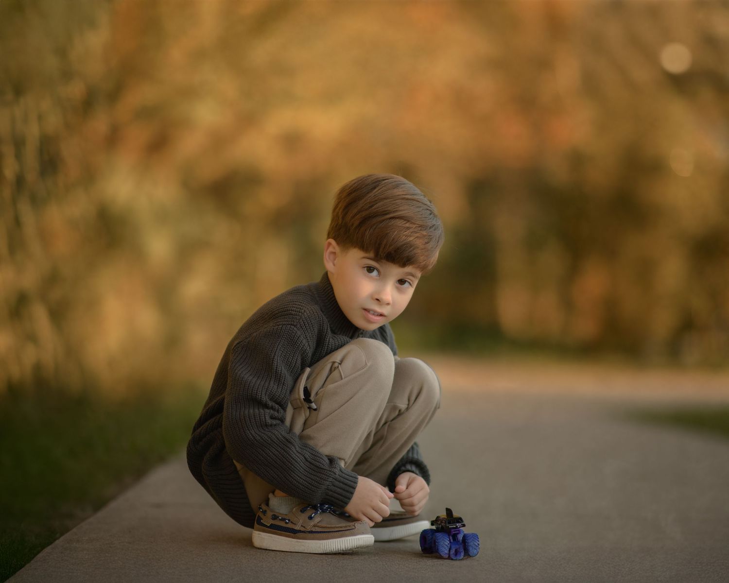 Playing with toy car on path surrounded by autumn foliage.