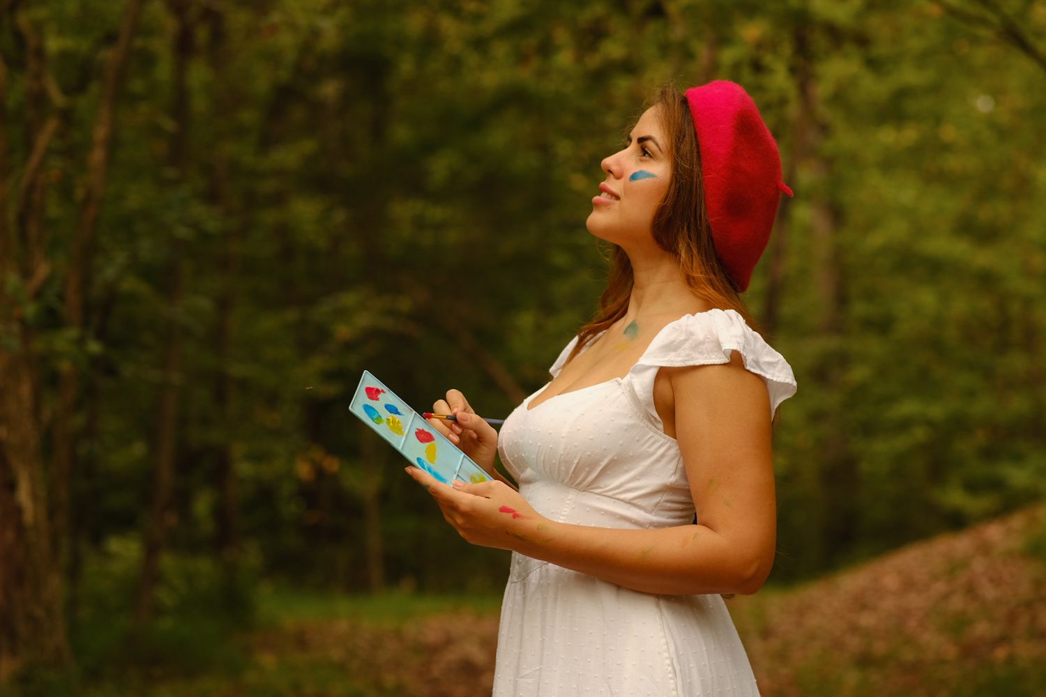 Woman in white dress and red beret reading book outdoors in woodland setting.