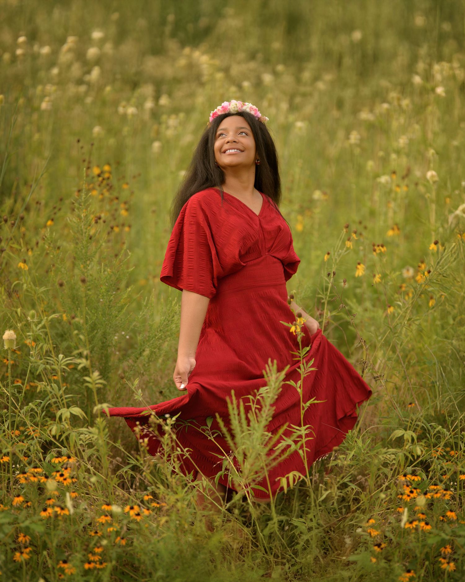 Someone in a flowing red dress and flower crown spins joyfully in a summer meadow filled with wildflowers.