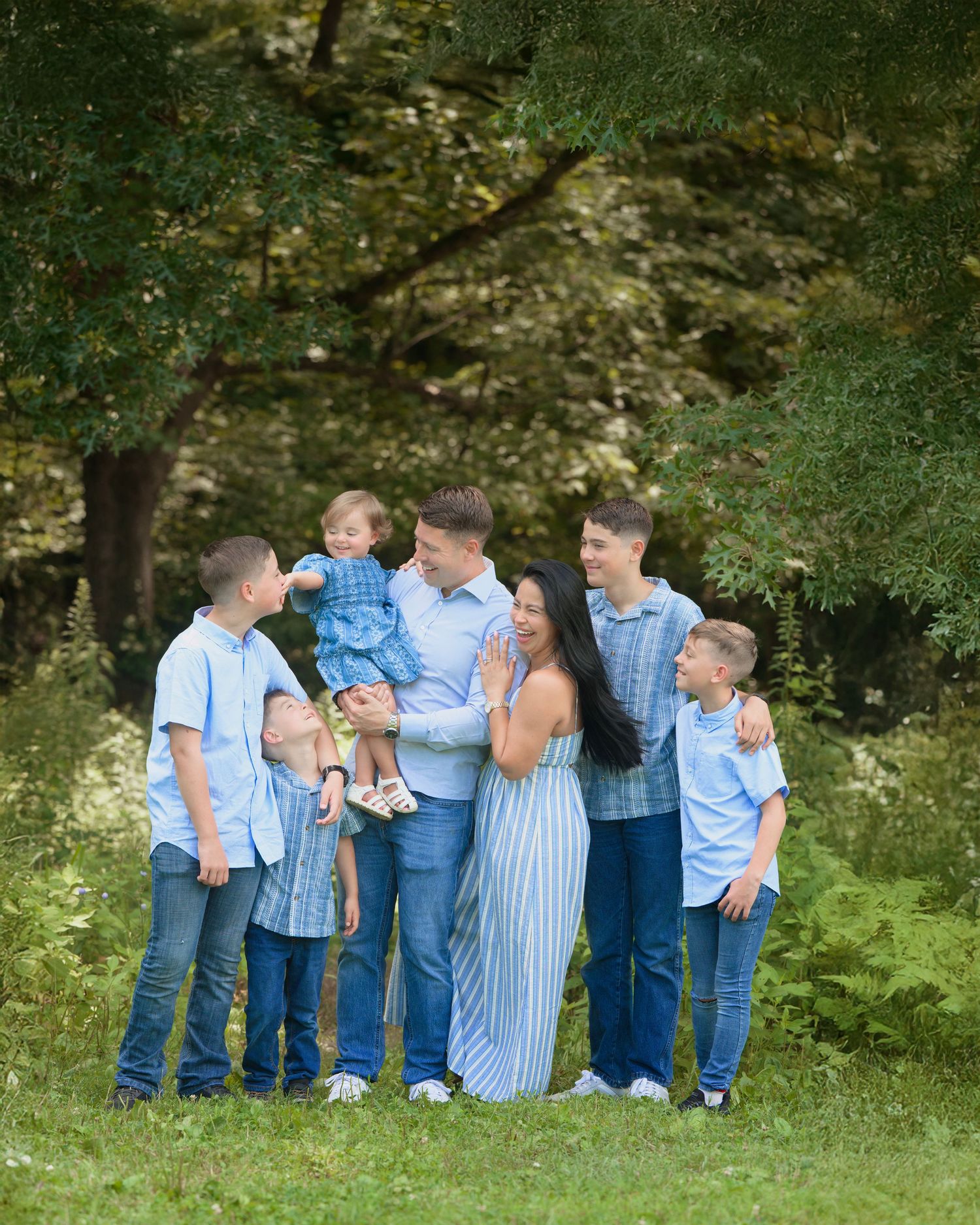 A group in coordinating blue and white outfits stands together on grass with trees in the background.