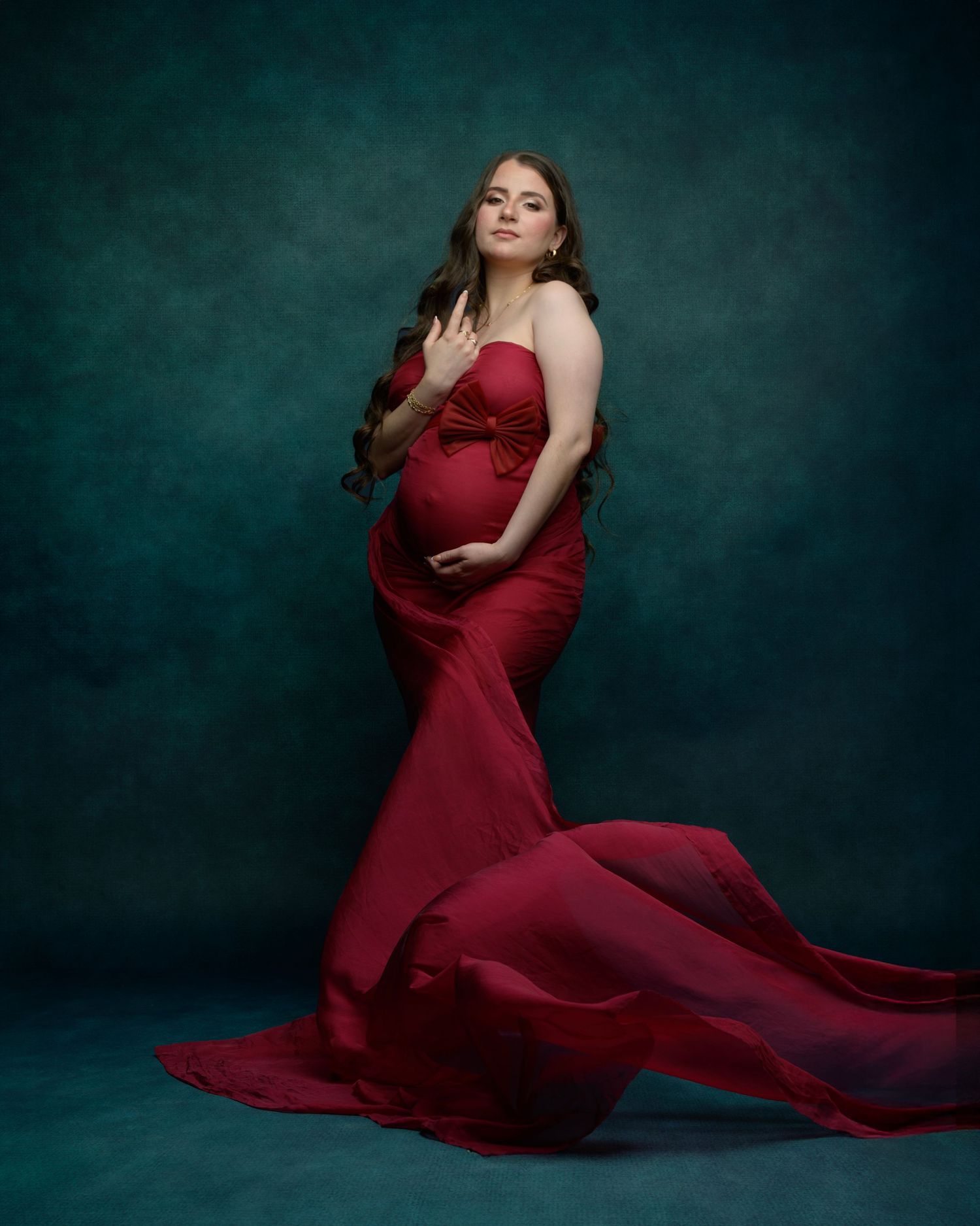 Maternity portrait of woman in flowing red gown against dark green background.