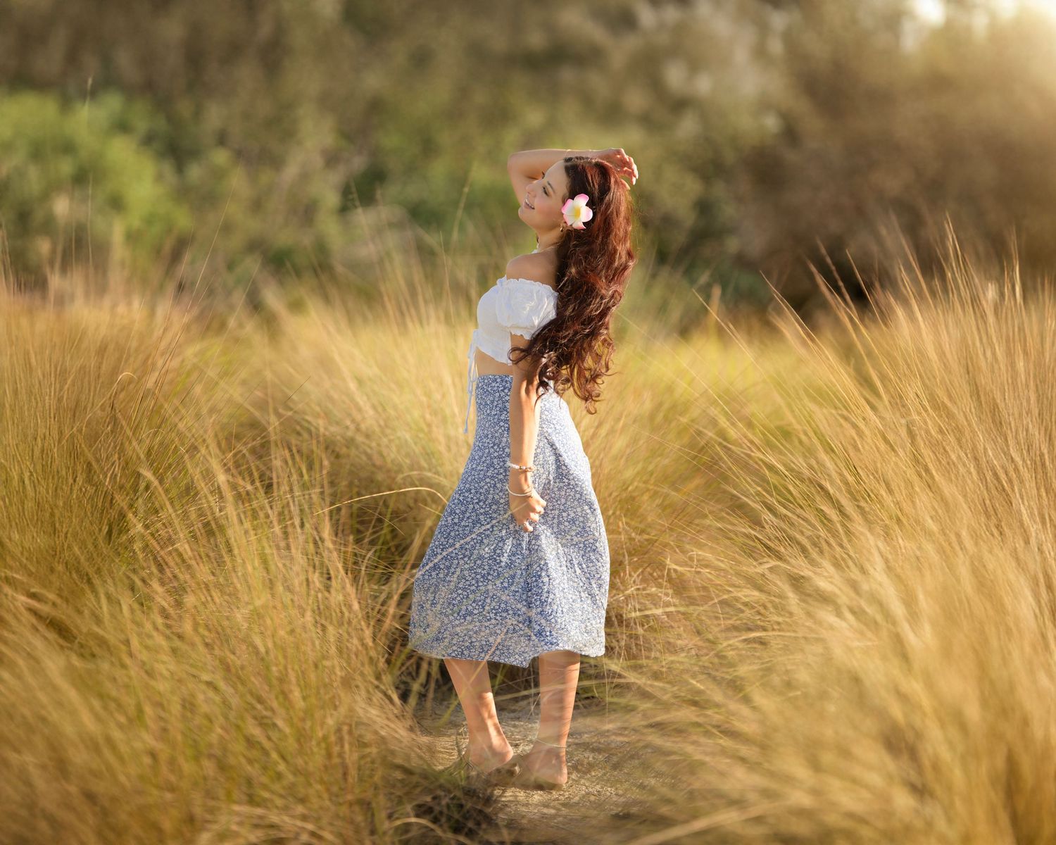 Person in flowing dress stands in golden sunlit field of tall grass.
