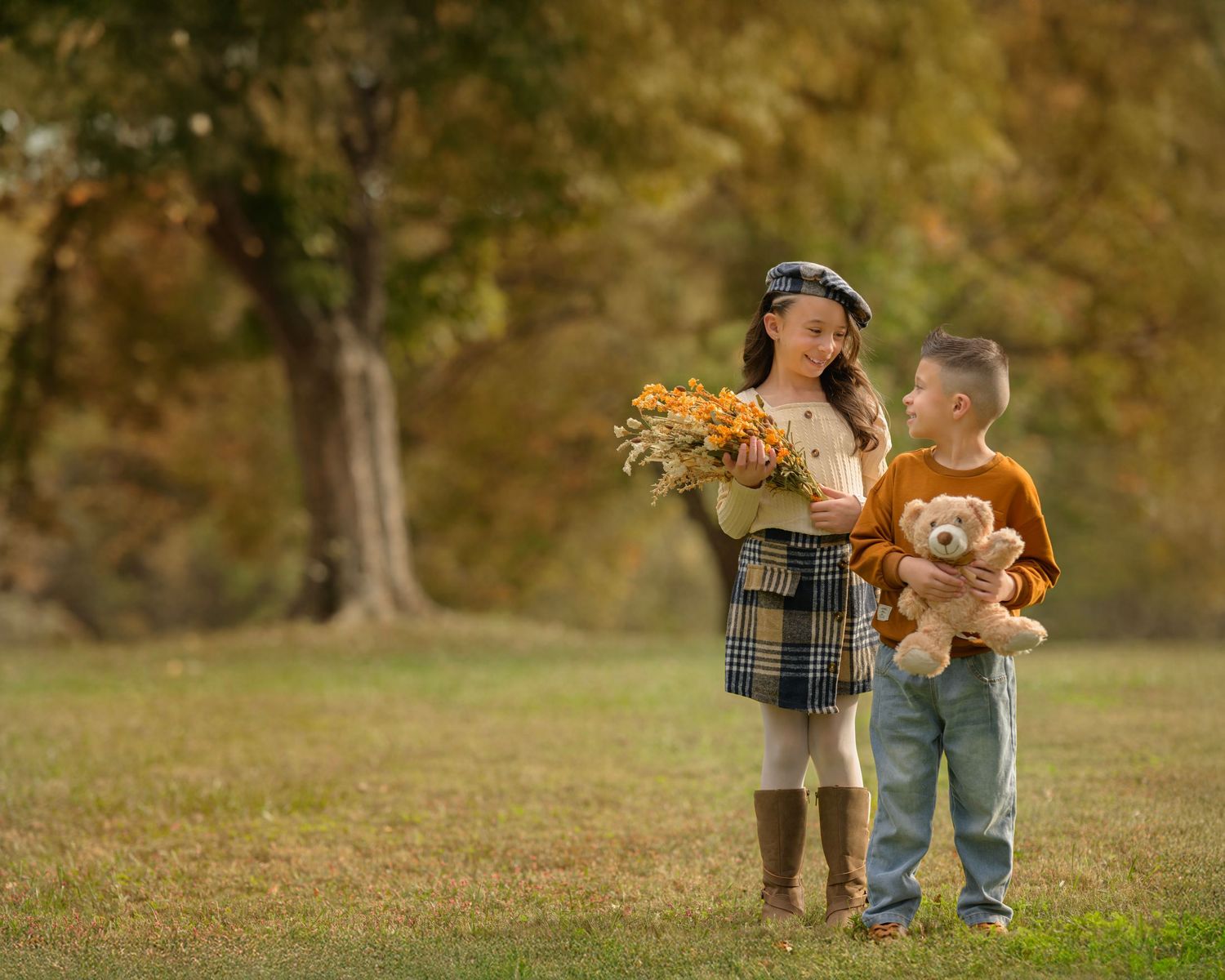 A couple walking their small brown dog through a park with golden autumn leaves on a sunny afternoon.