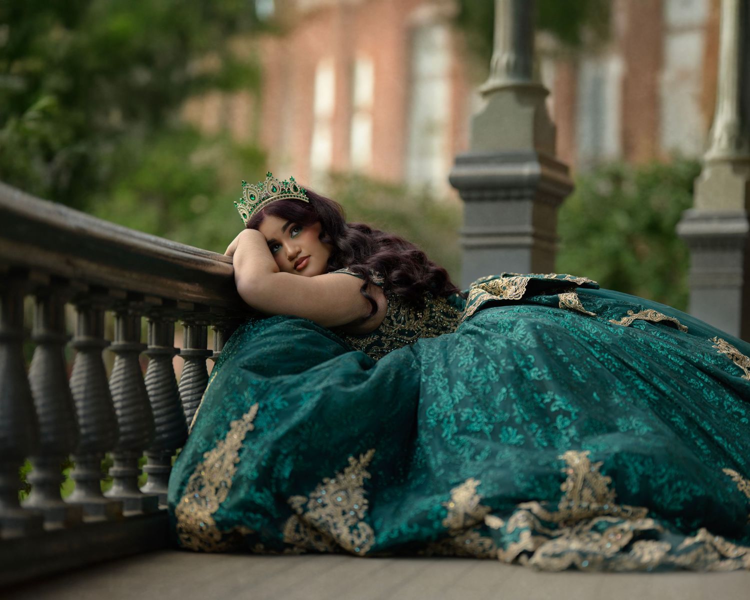 Romantic portrait in emerald gown resting on ornate balcony railing.