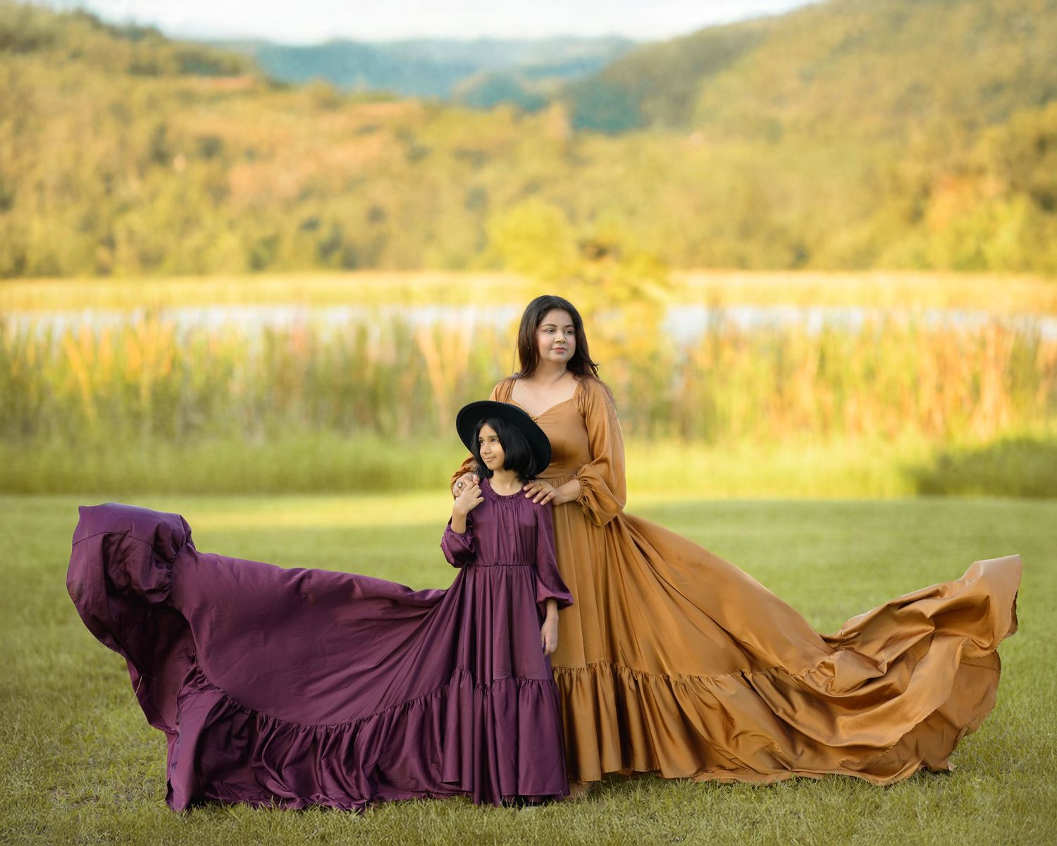 Two flowing dresses in brown and purple billow dramatically in a meadow with autumn mountains in the background.