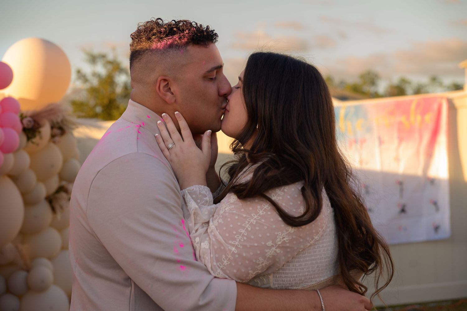 Couple sharing intimate kiss at celebration with balloon decorations in background.