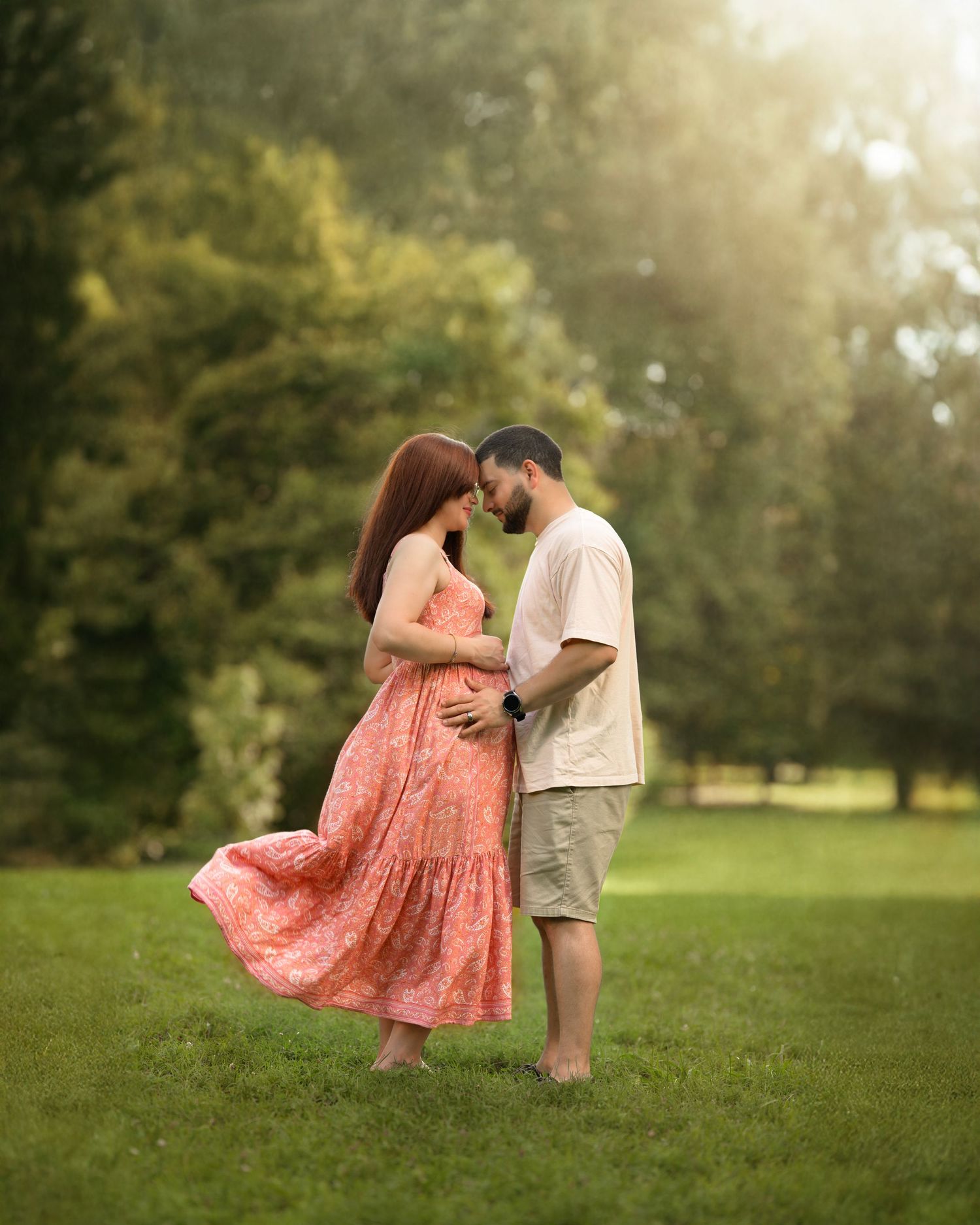 A couple dances together outdoors on green grass with sunlit trees in the background during golden hour.