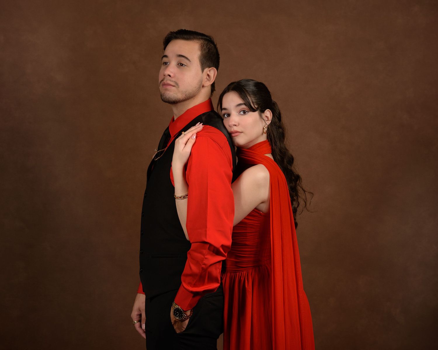A romantic couple in formal attire dances together, with the woman wearing a flowing red dress against a dark brown backdrop.