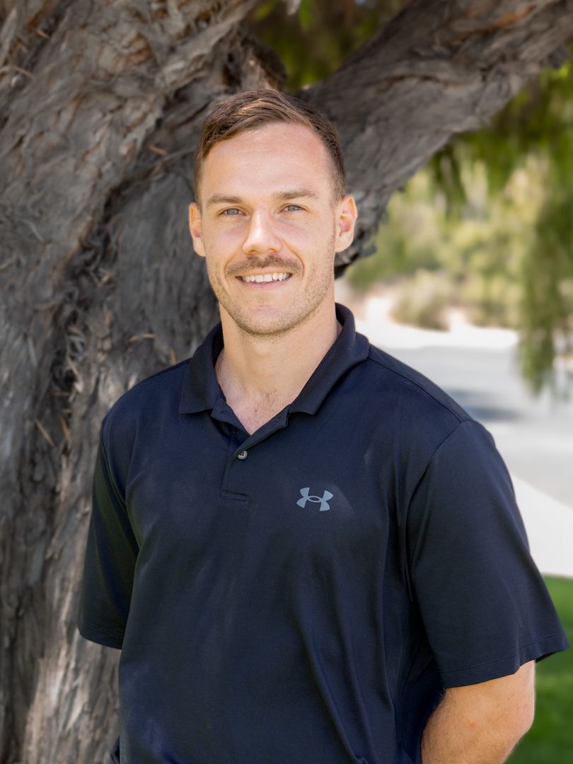Person wearing a black Under Armour polo shirt poses outdoors against a tree backdrop in natural lighting.