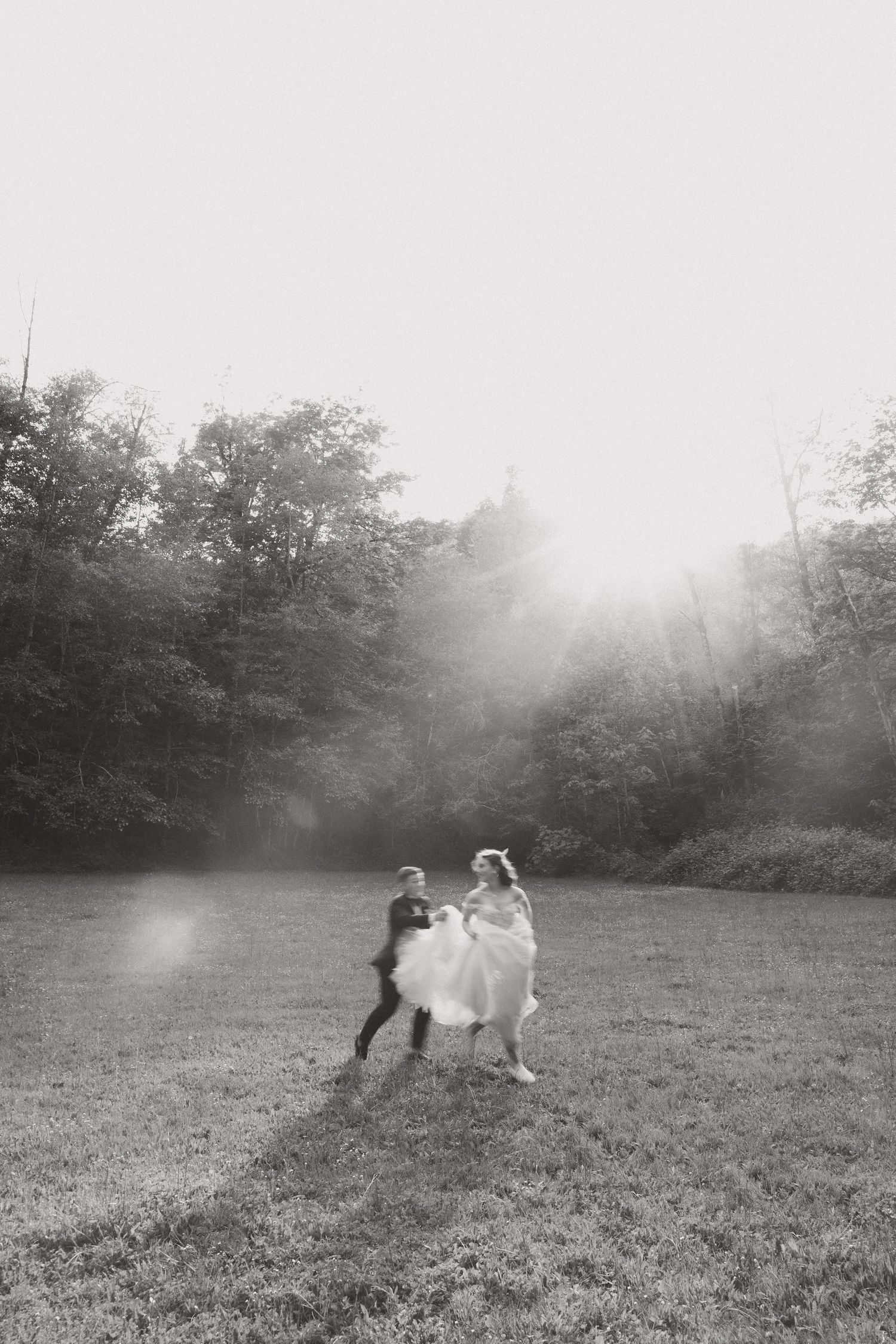 Candid editorial style wedding photography at Camp Lane Oregon of bride and groom playfully dancing in a sunlit field surrounded by trees.