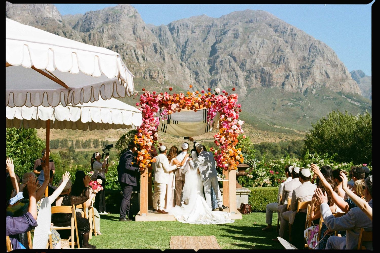 Outdoor wedding ceremony setup with floral arch against dramatic mountain landscape.
