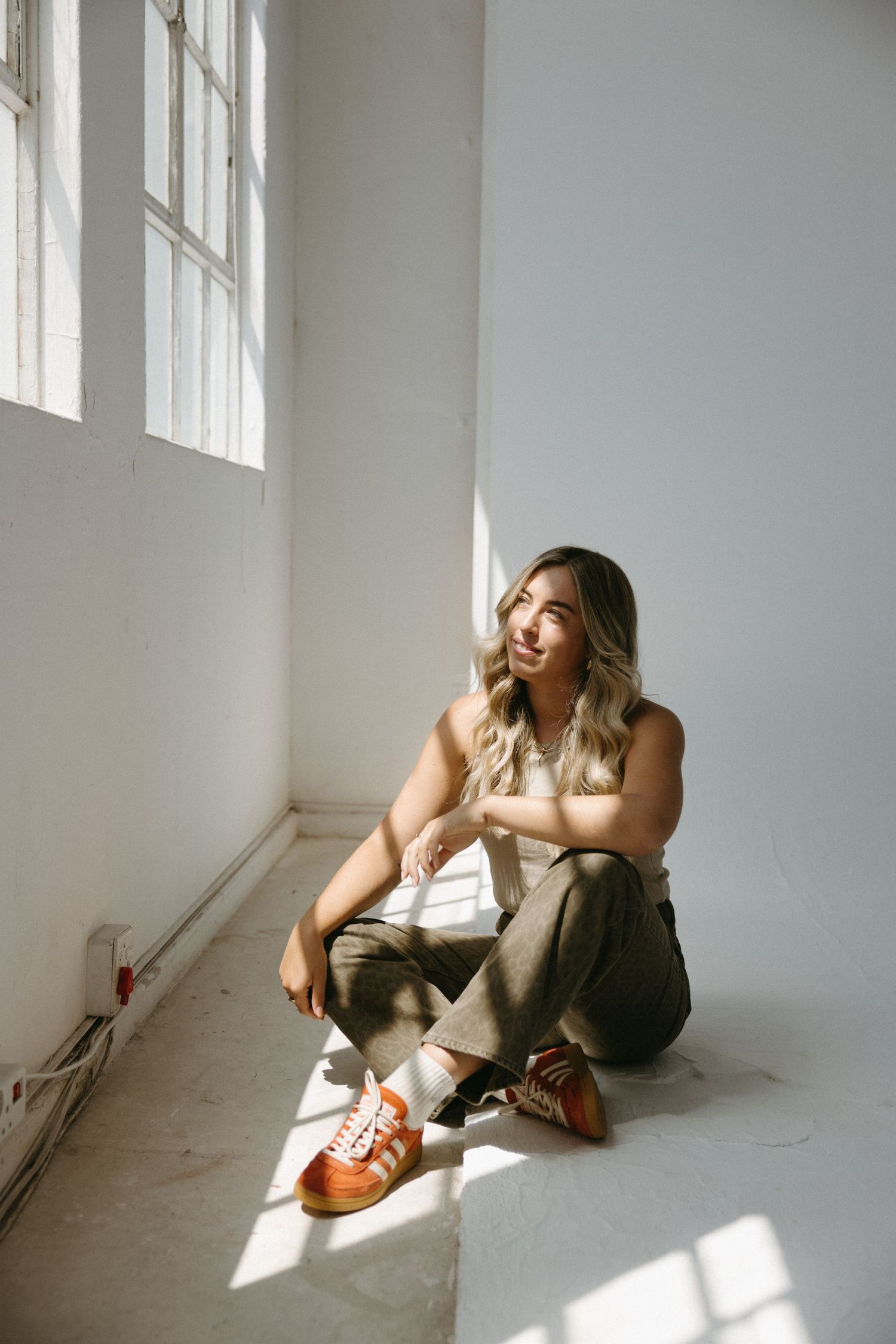 Person sitting casually on floor by window wearing brown pants and leather shoes as natural light streams in.