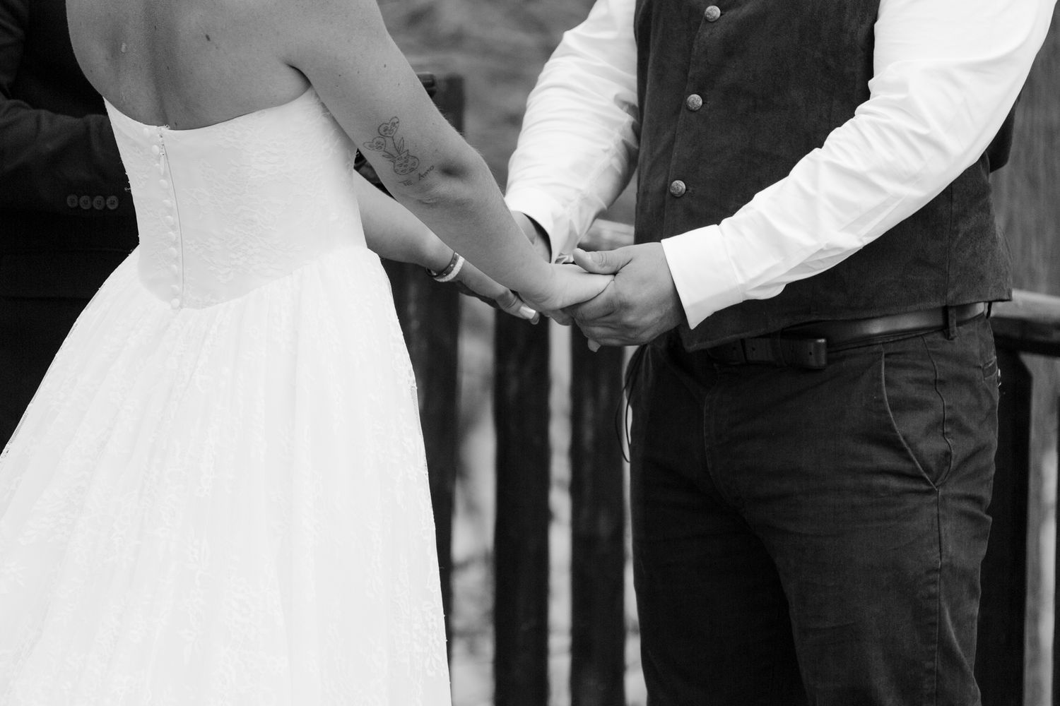 Black and white photo of bride and groom holding hands during wedding ceremony outdoors.