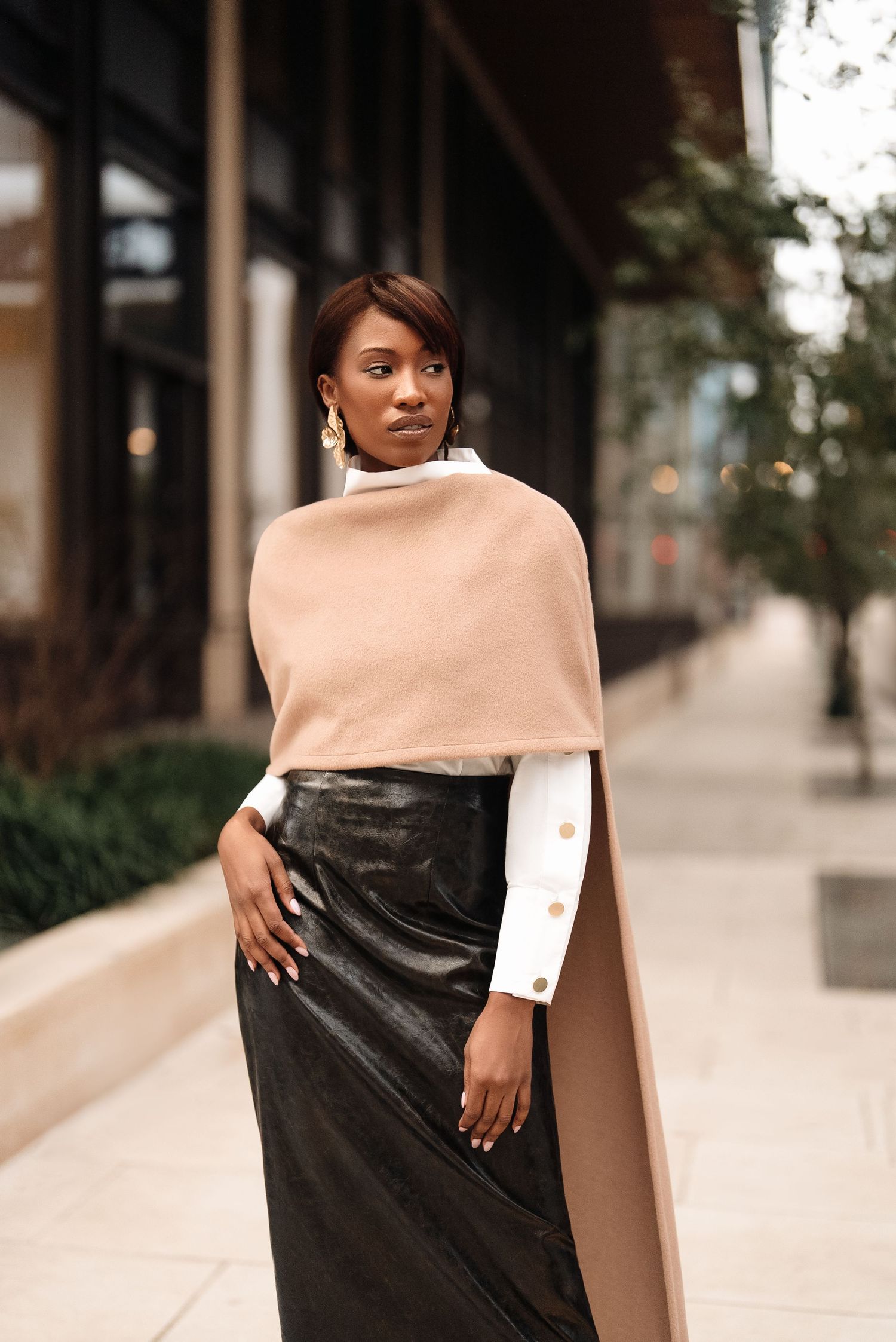Street style fashion shot featuring cream cape and black leather skirt ensemble.