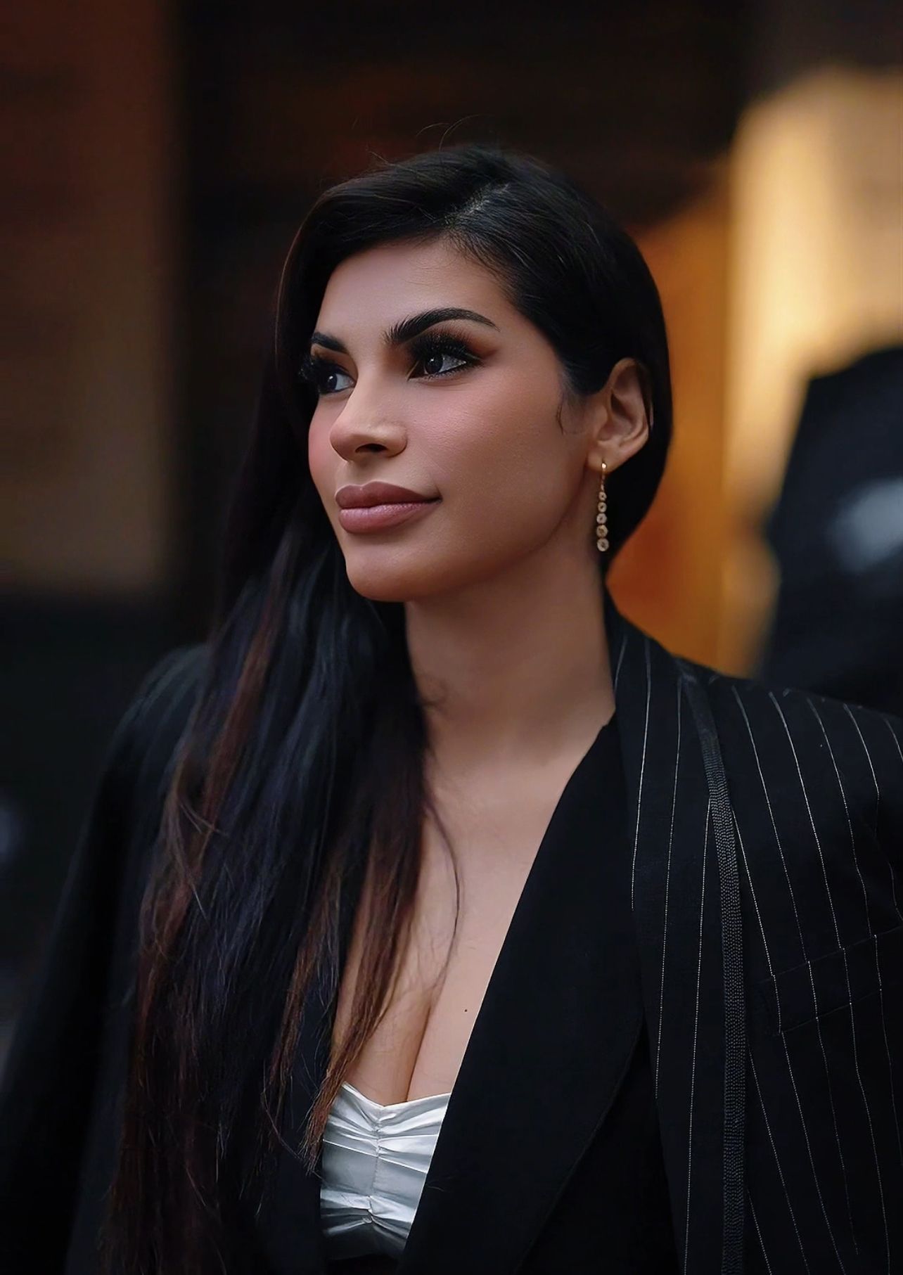 A professional portrait featuring dark pinstripe blazer and long black hair against a warm blurred background.