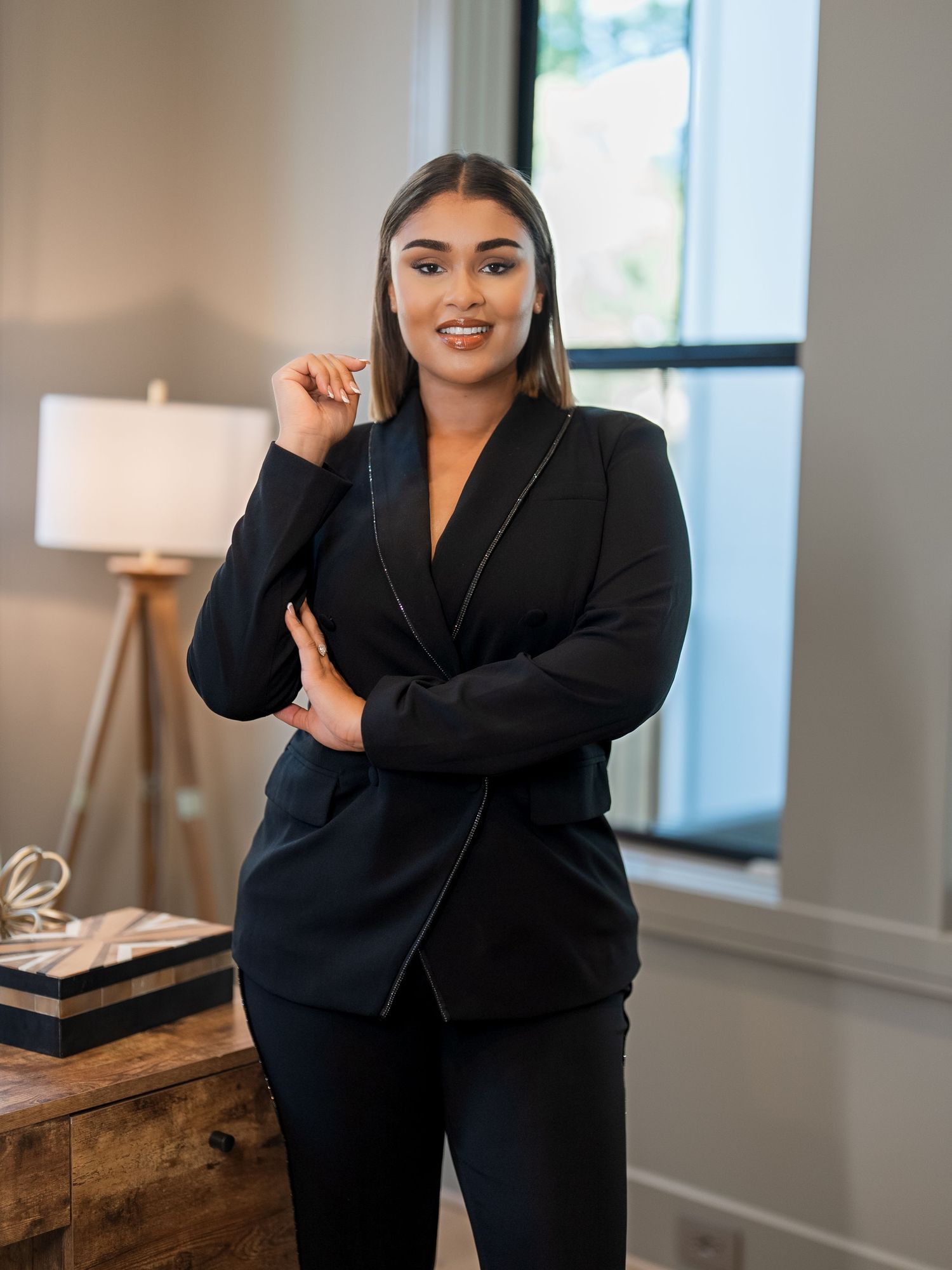 Professional portrait of woman in black business suit standing in modern office setting.