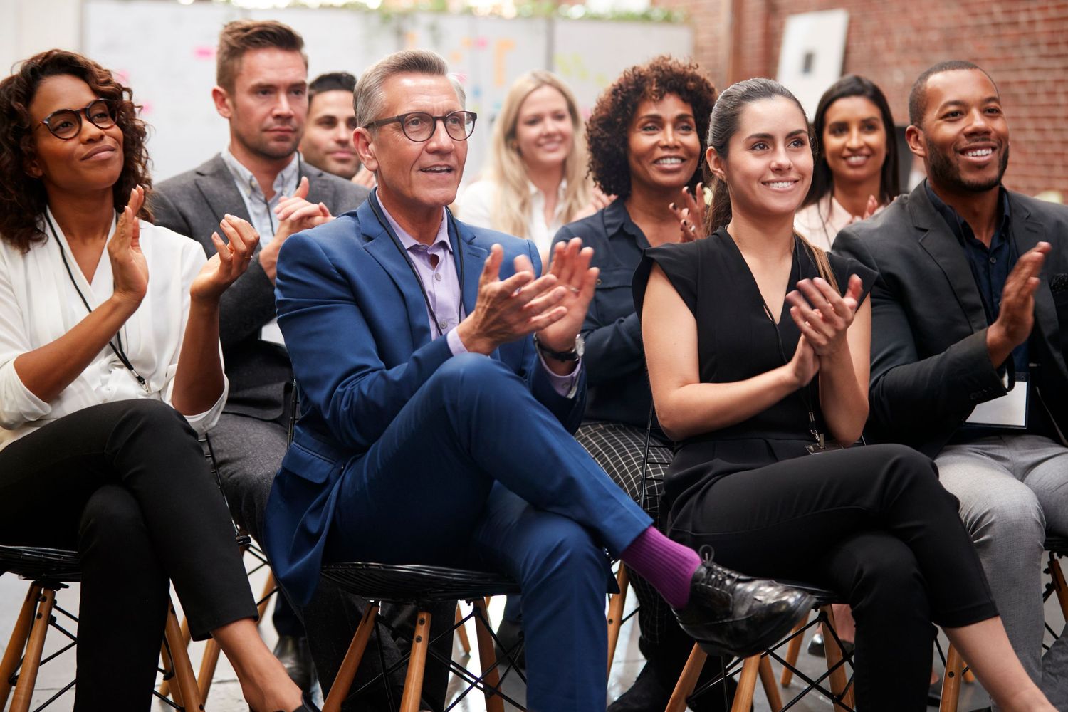 Diverse group of professionals seated in a row applauding at a business conference or presentation.
