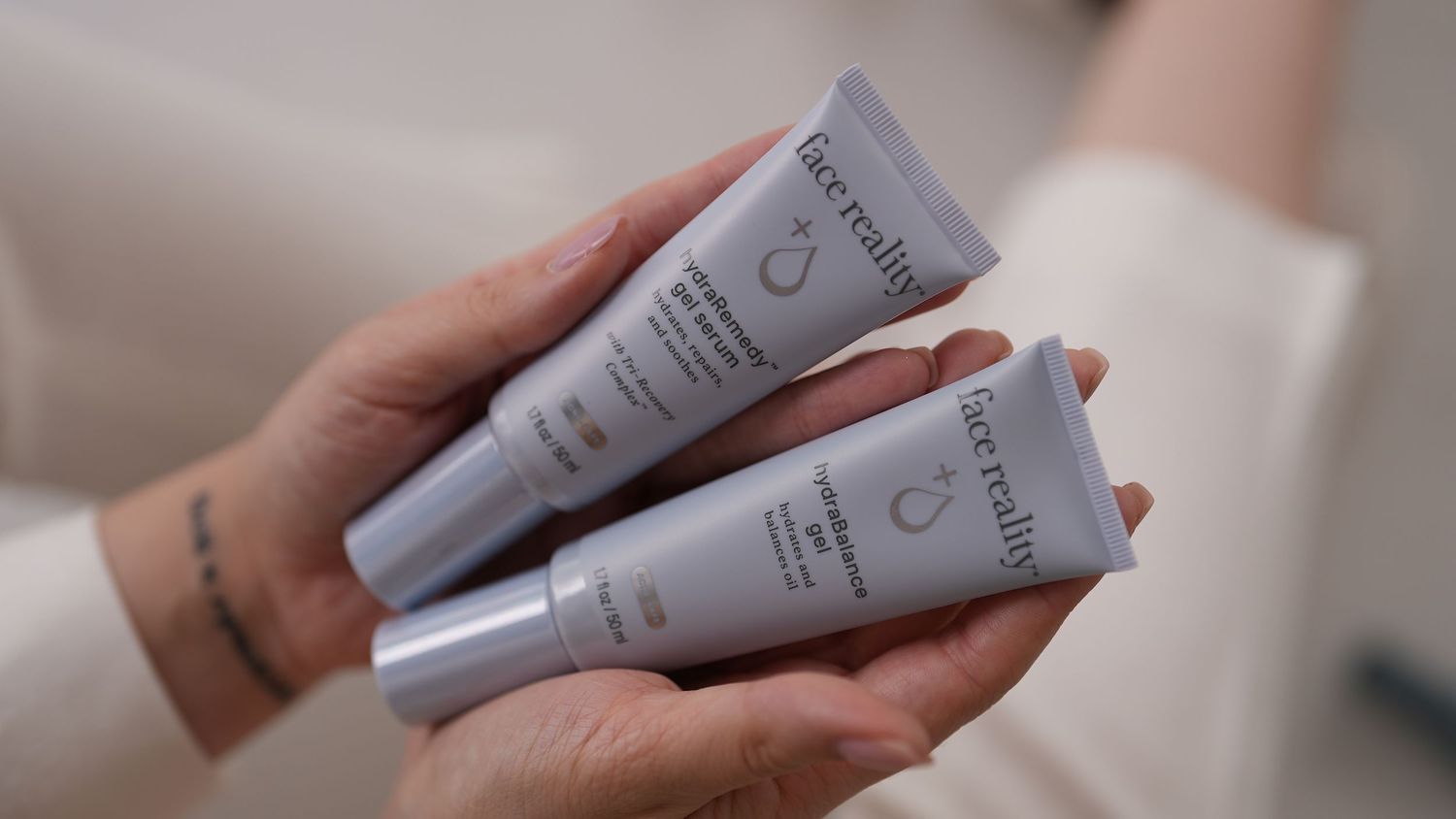 Two skincare product tubes being held in hands against light background.
