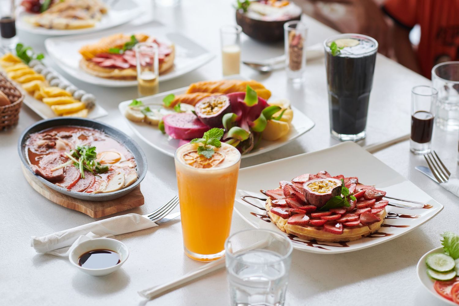 A spread of colorful brunch dishes and drinks on a white table setting.