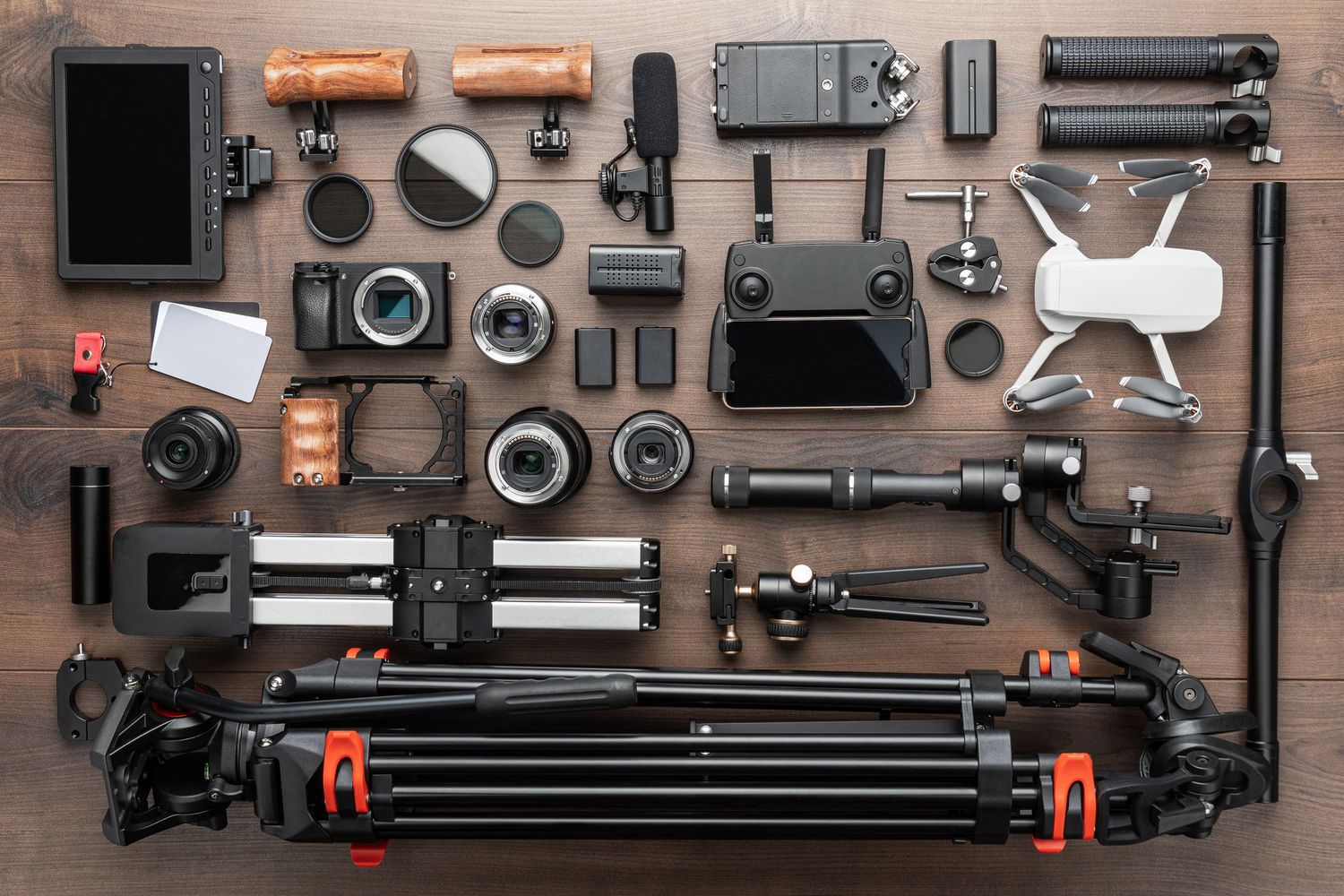 Professional photography and drone equipment neatly arranged on wooden surface including cameras, lenses and tripods.