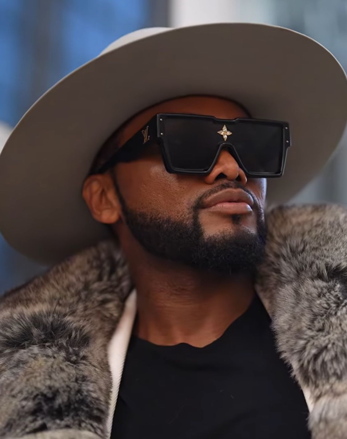 Stylish person wearing sunglasses, wide-brim hat and fur coat in an urban setting.