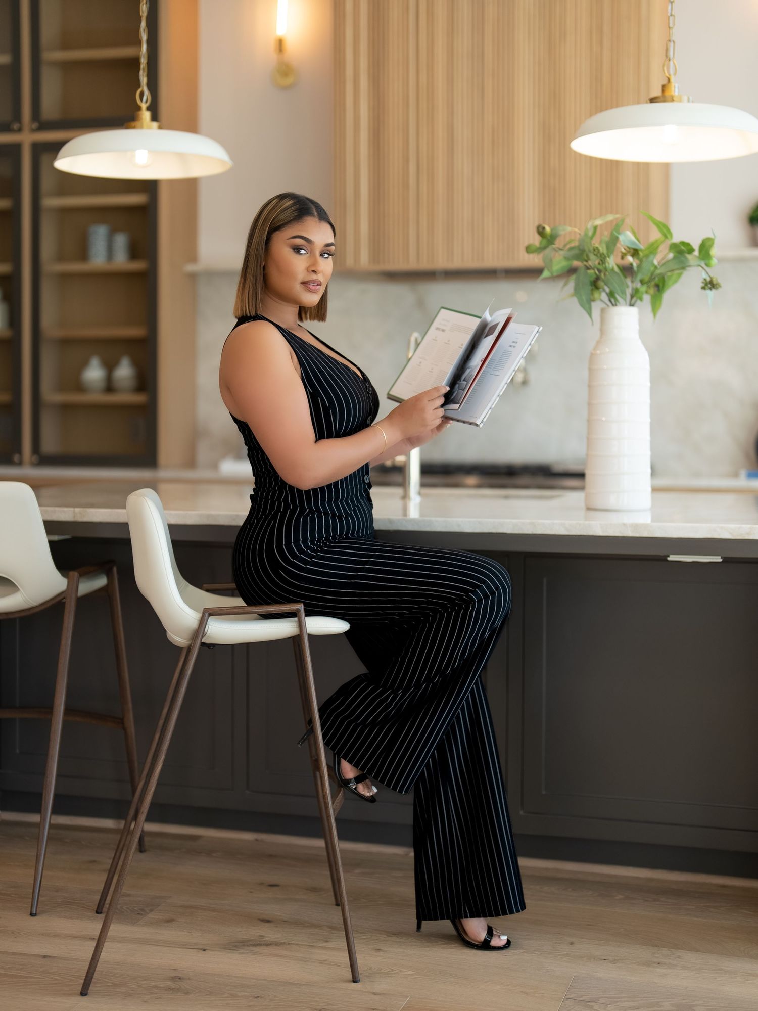 Professional woman in pinstripe jumpsuit reading while seated at modern kitchen counter.