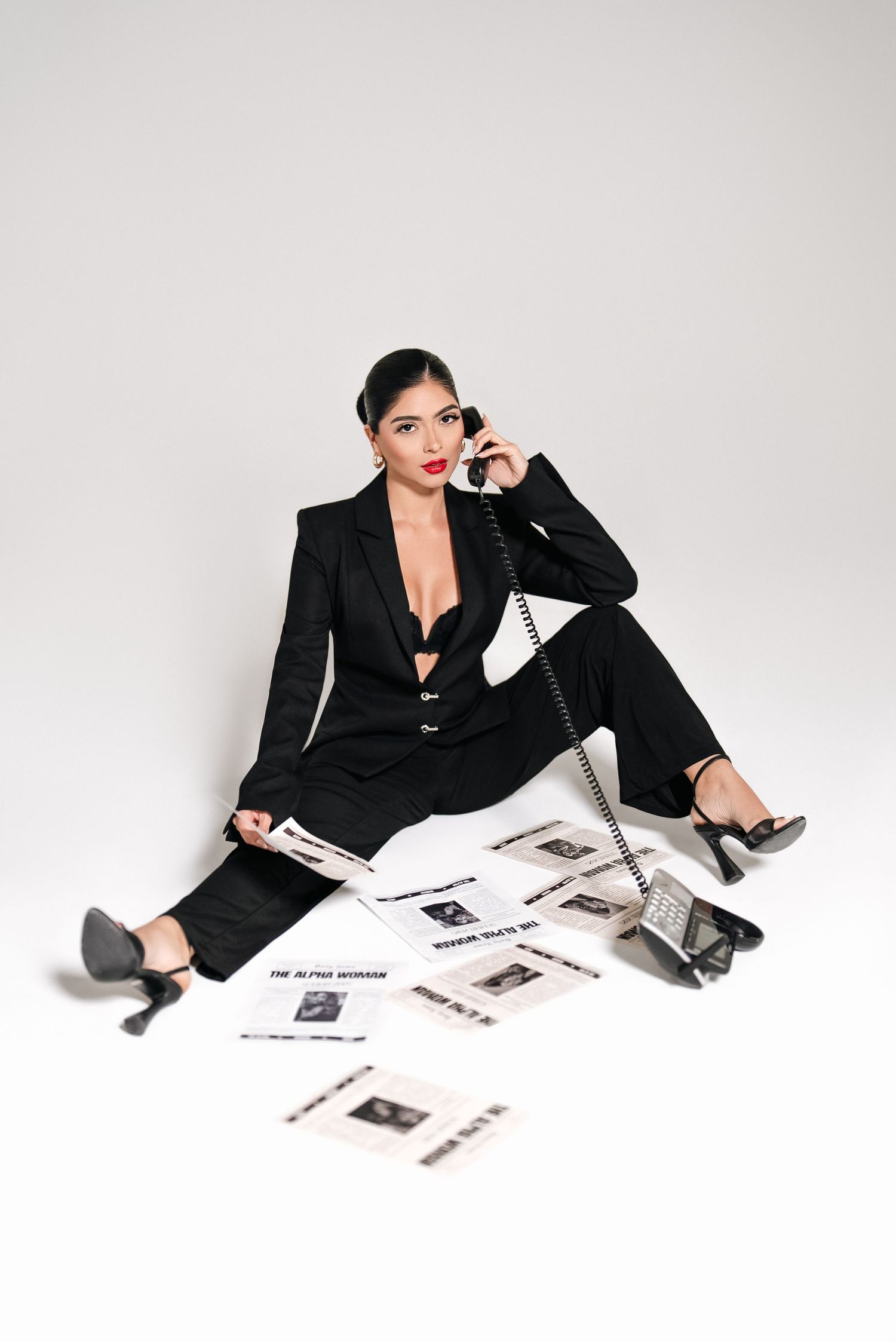 Stylish business look with black suit and heels while sitting among scattered photographs.