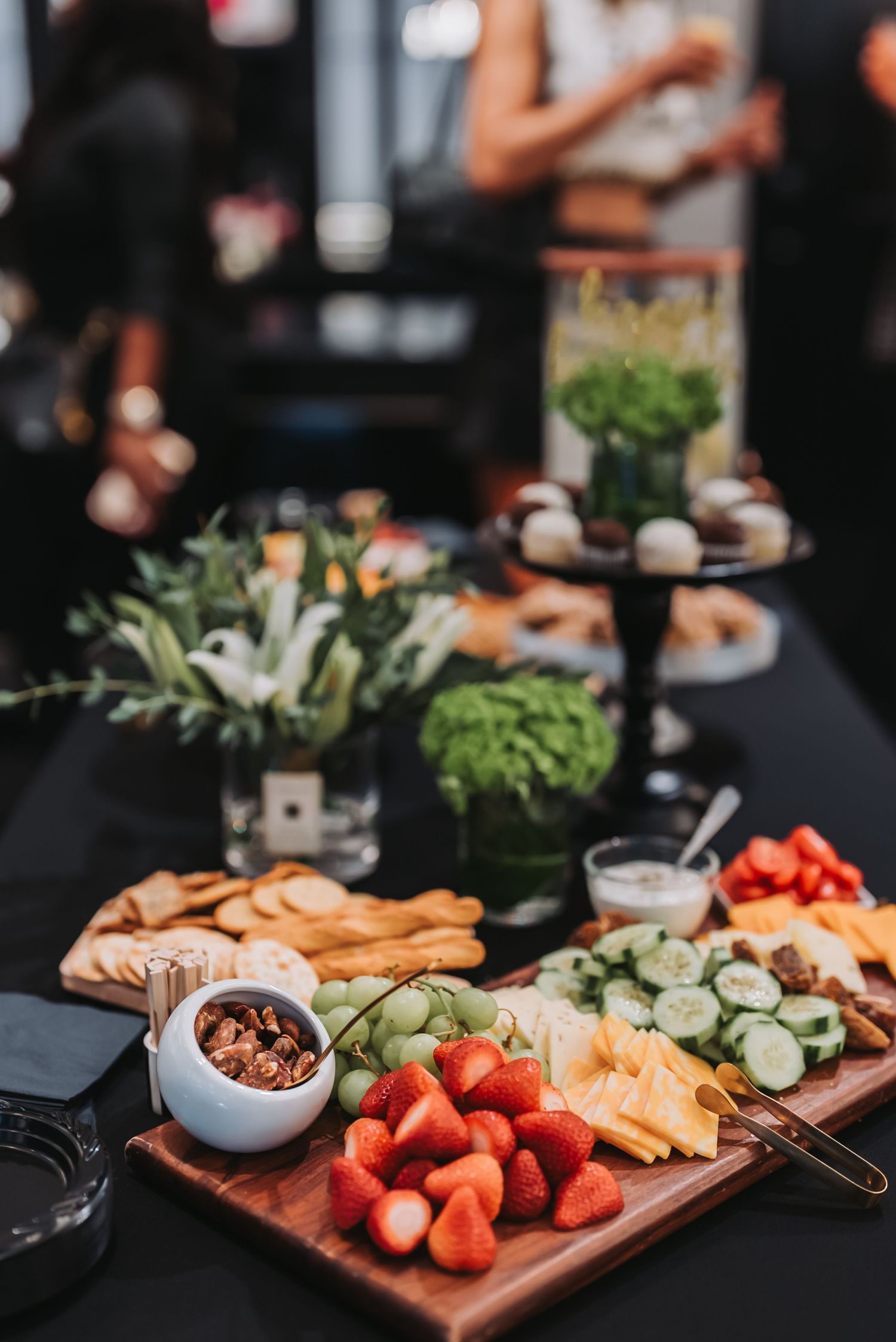 Appetizing charcuterie board with fresh fruits, vegetables, and snacks on dark table setting.