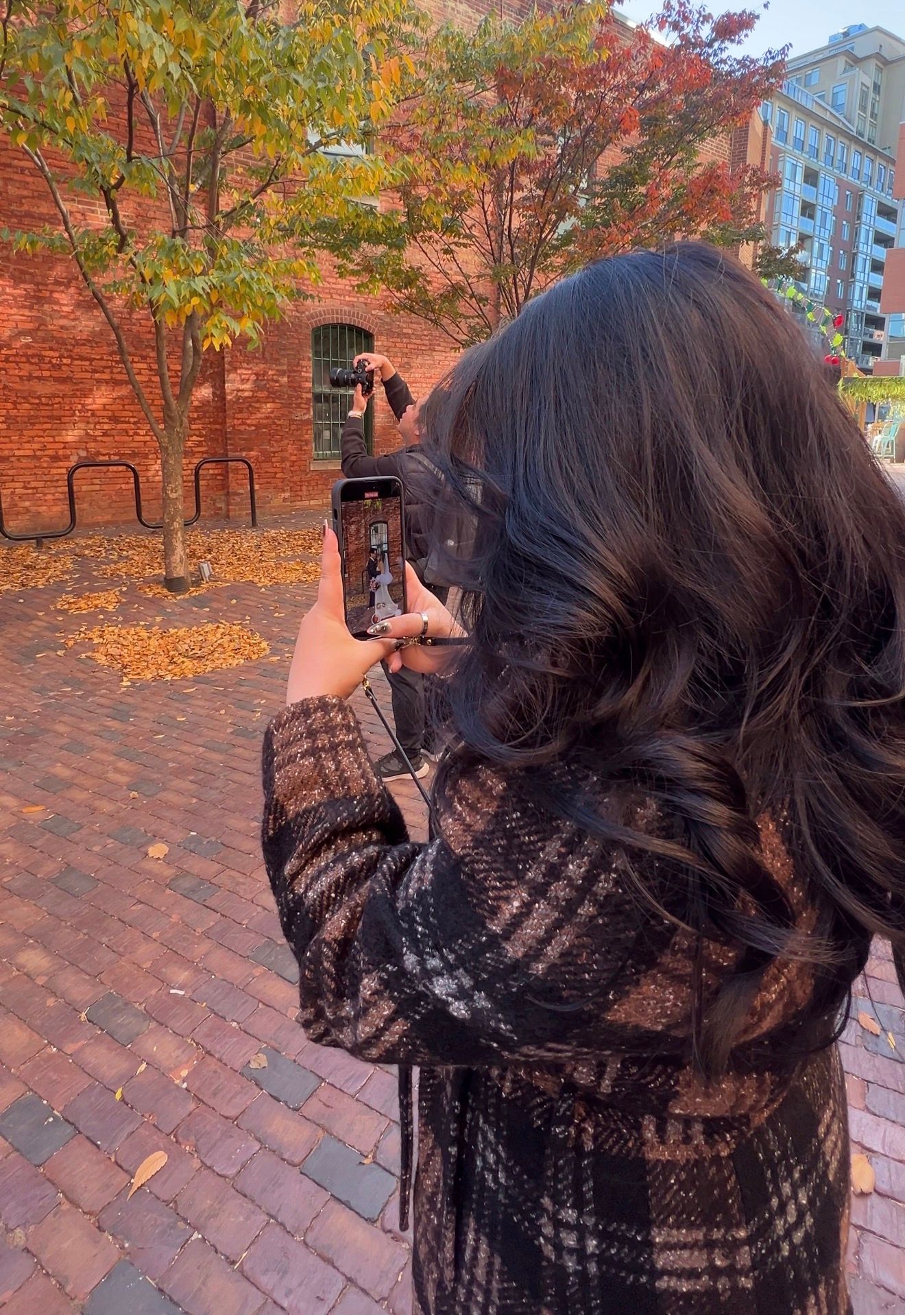 Person wearing black lace shawl poses against backdrop of vibrant autumn trees with orange and red foliage.