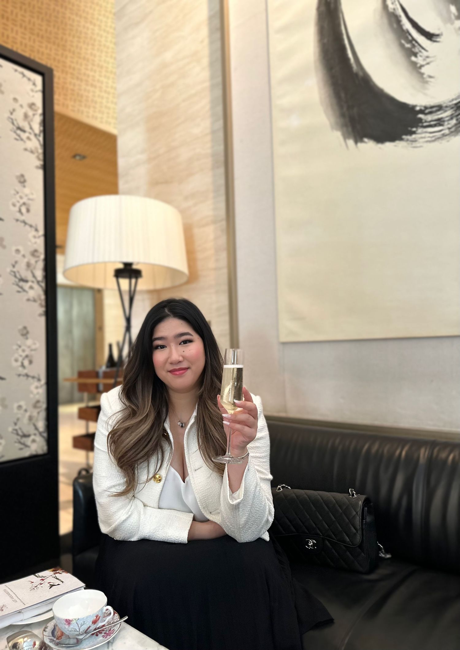 A person enjoying a glass of champagne while sitting on a leather couch in an elegant lounge with art on the walls.
