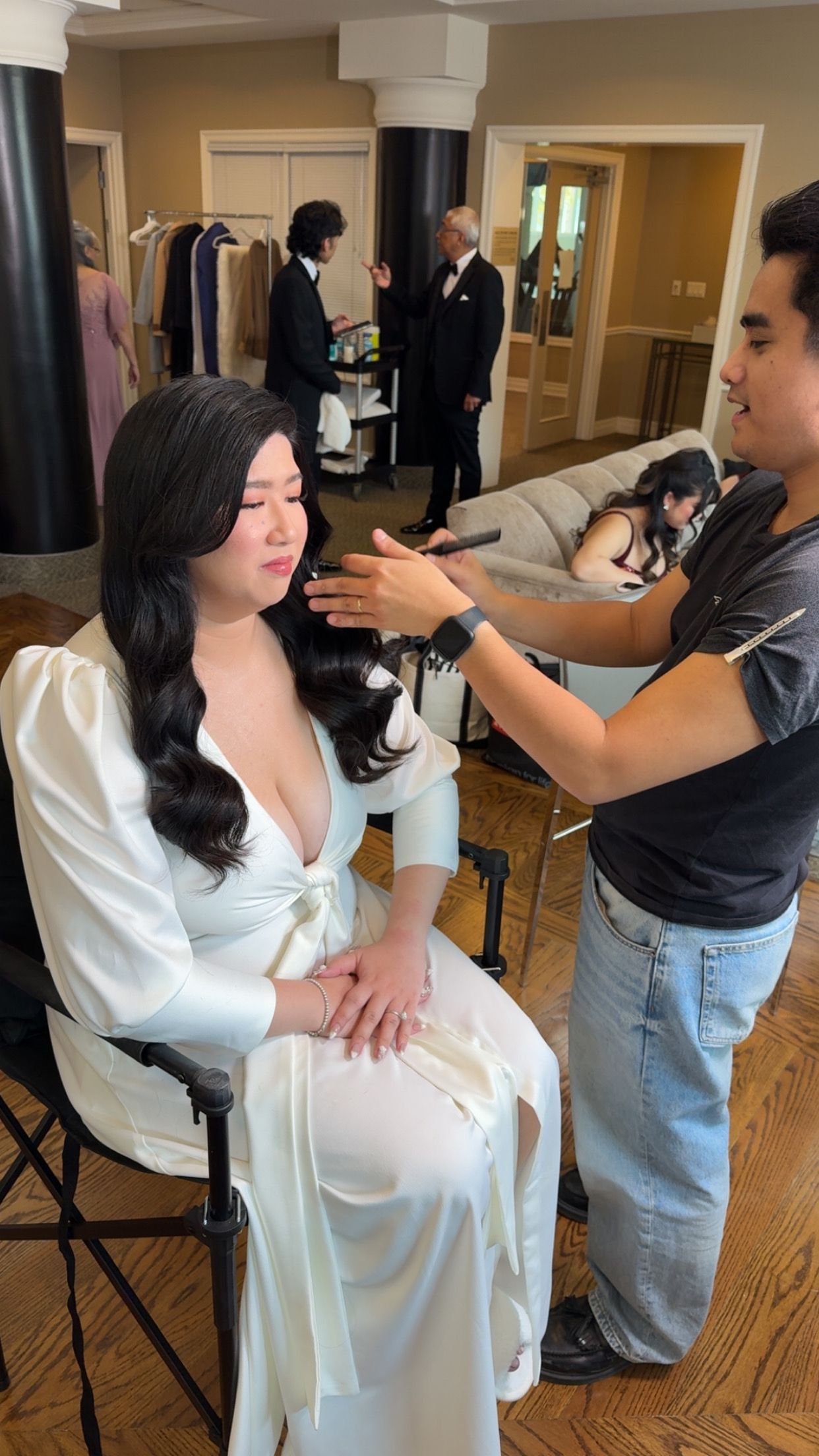 Makeup artist applies finishing touches to a person in a white robe during a beauty preparation session.