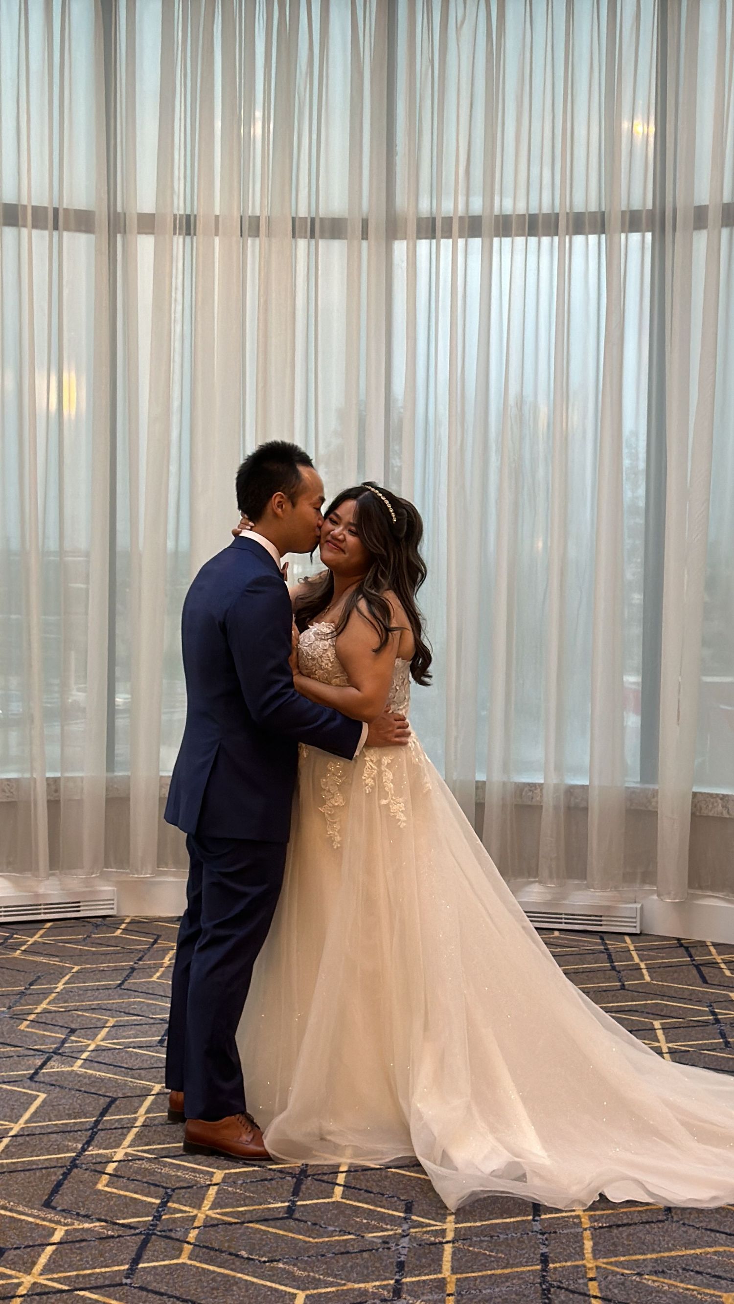 Newlyweds share an intimate moment in front of sheer curtains with bride wearing a flowing champagne wedding gown.