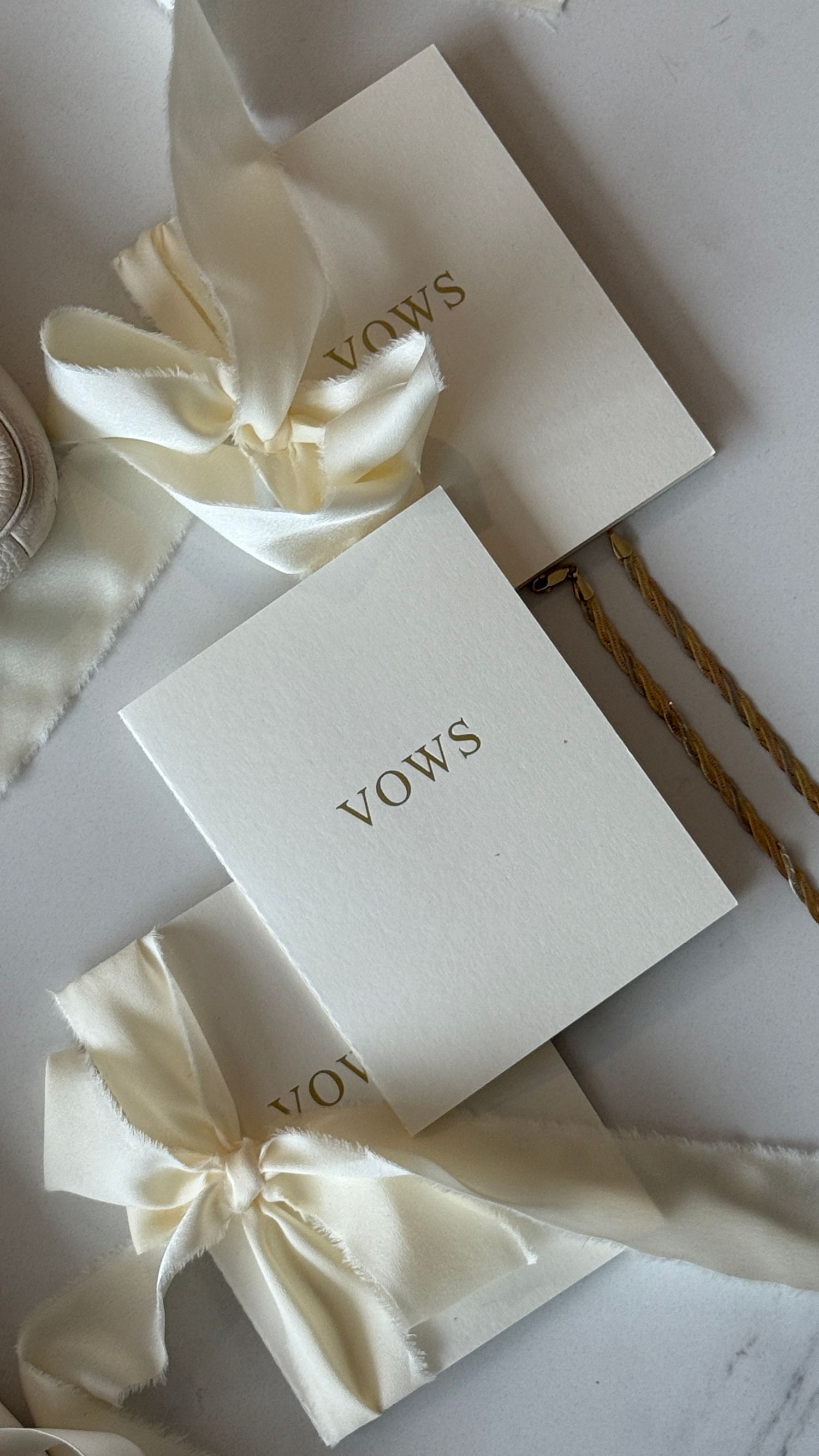 White vow cards with cream silk bows arranged on a marble surface for wedding ceremony preparation.