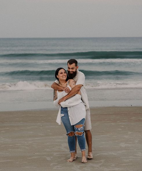 A joyful couple embracing on a sandy beach with ocean waves in the background.
